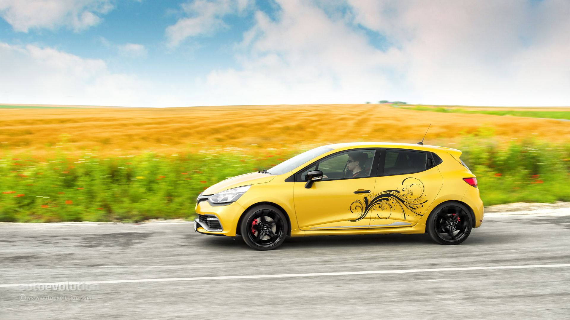 Renault 桌布 壁紙 — 一輛充滿活力的黃色雷諾Clio跑車在鄉村道路上疾馳，背景是動態模糊的金色田野和藍天。