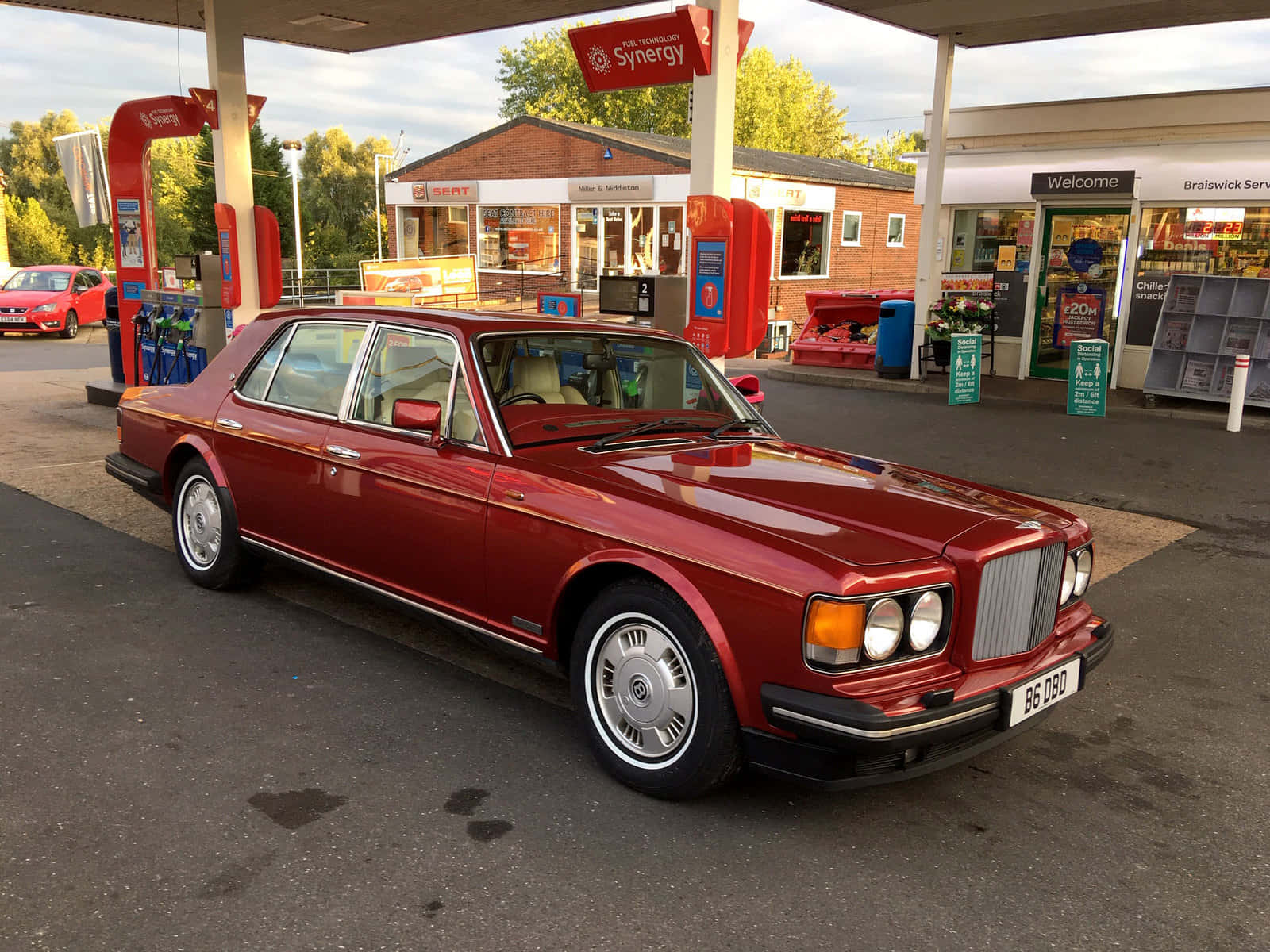 Bentley Eight 桌布 壁紙 — 一輛光亮的紅色 Bentley Turbo R 停泊在加油站，背景有便利商店和樹木。