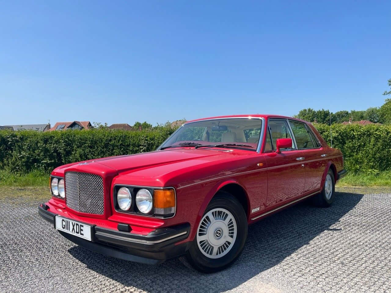 Bentley Eight 桌布 壁紙 — 一輛光亮的紅色 Bentley Turbo R 在陽光明媚的碎石車道上閃閃發光，車道兩旁是綠色樹籬。