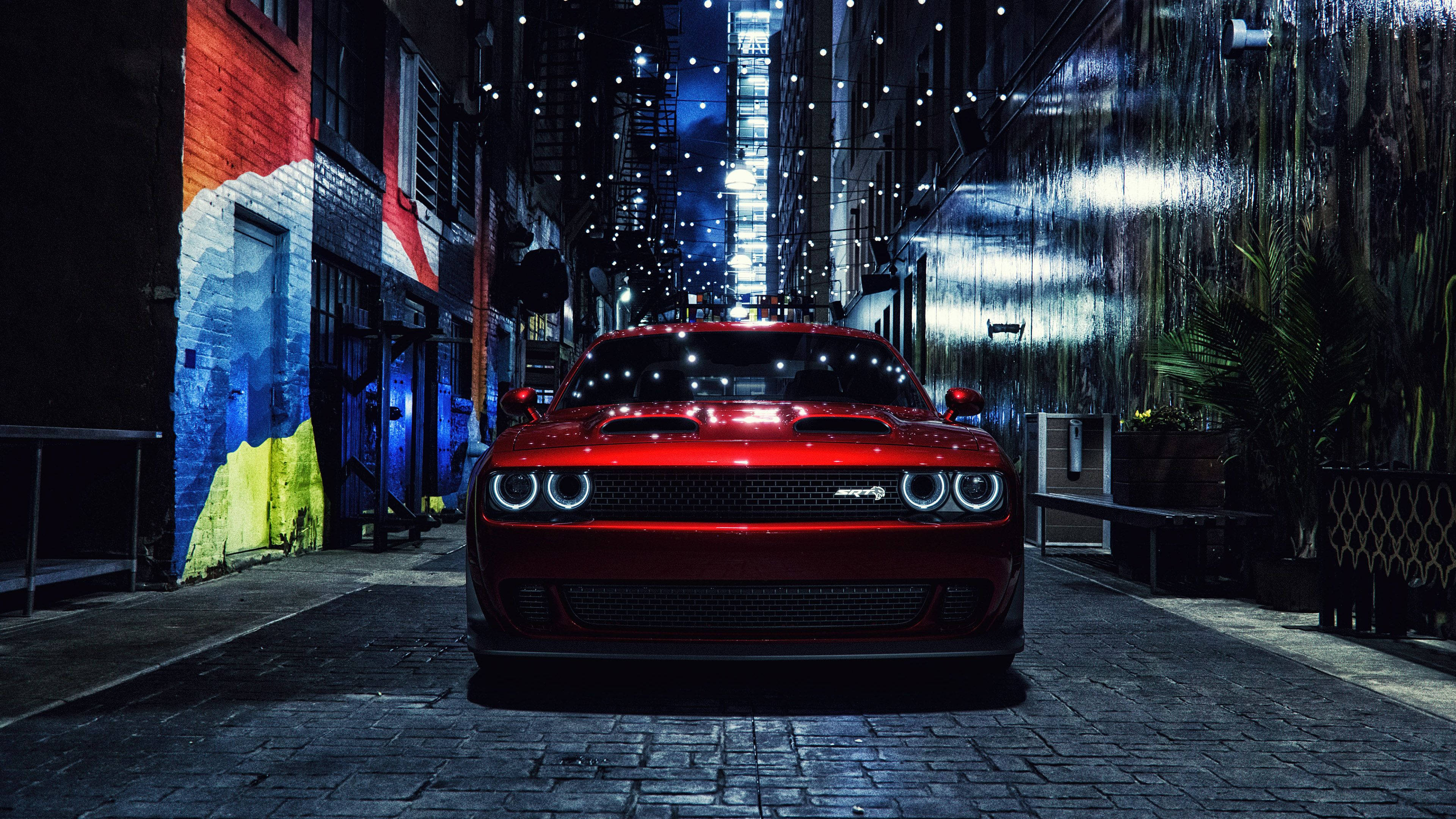 Challenger 桌布 壁紙 — 一輛光亮的紅色 Dodge Challenger SRT Hellcat 在夜間主宰著一條狹窄的城市小巷，兩旁是色彩繽紛的壁畫和串燈，倒映在濕漉漉的鵝卵石上。