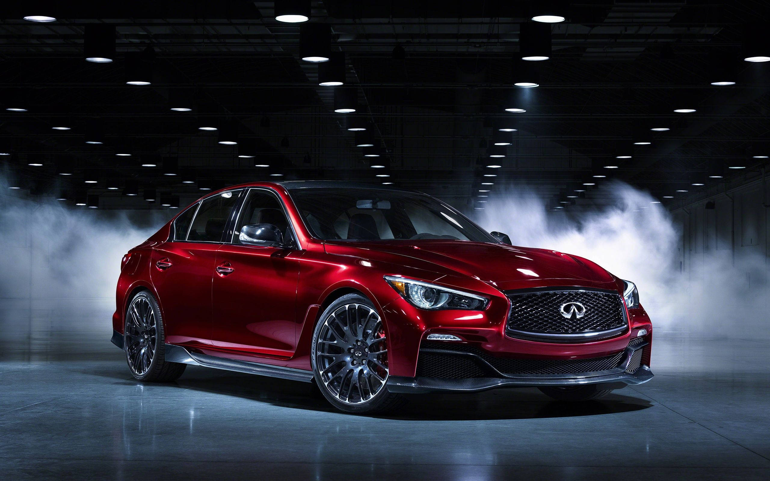 Infiniti 桌布 壁紙 — 一輛光亮的紅色 Infiniti 轎車在黑暗的工業機庫中，於旋轉的煙霧中在攝影棚燈光下閃閃發光。