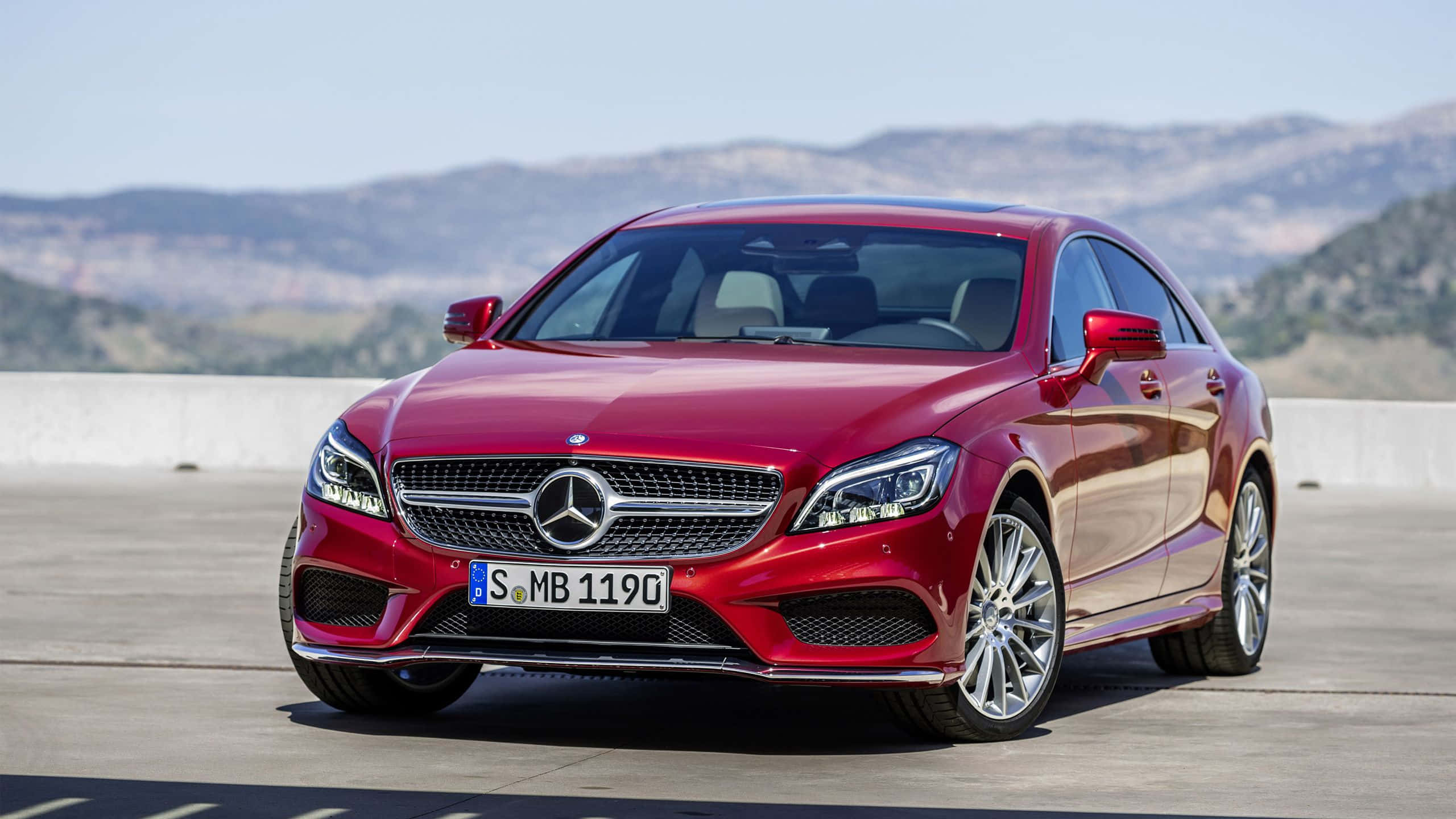 跑車 桌布 壁紙 — 一輛光亮的紅色 Mercedes-Benz CLS Coupe 在明亮的陽光下，在混凝土觀景台上閃閃發光，背景是起伏的丘陵。