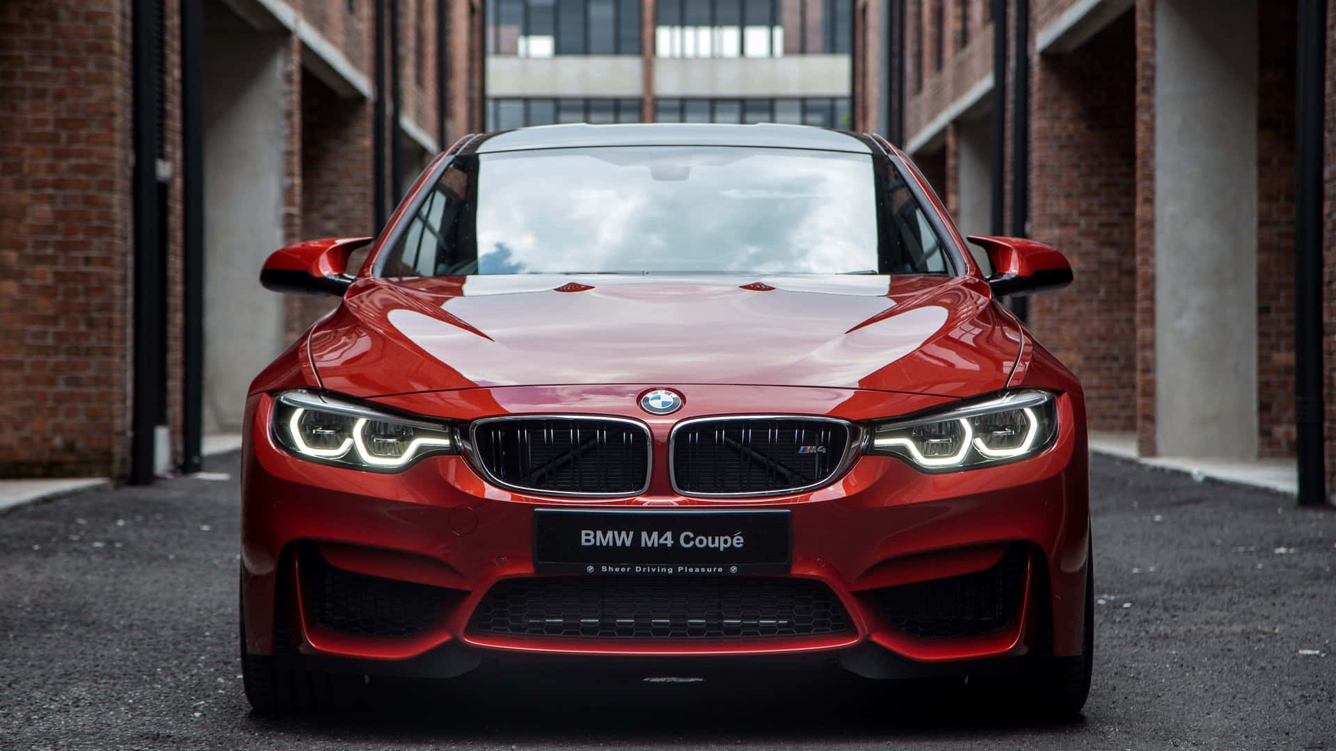 紅色BMW M4 Coupe停在磚砌建築之間的瀝青街道上。 — Toyota Supra Mk4 壁紙