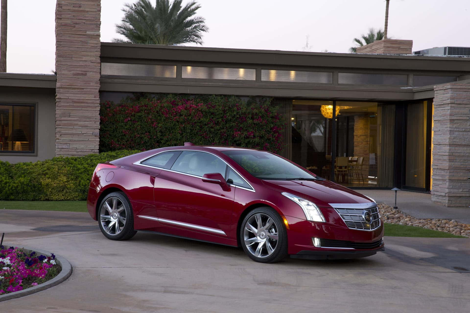Cadillac Elr 桌布 壁紙 — 一輛光亮的紅色Cadillac ELR雙門轎跑車停放在現代化住宅前的鋪砌車道上，住宅周圍有棕櫚樹和開花的灌木叢。