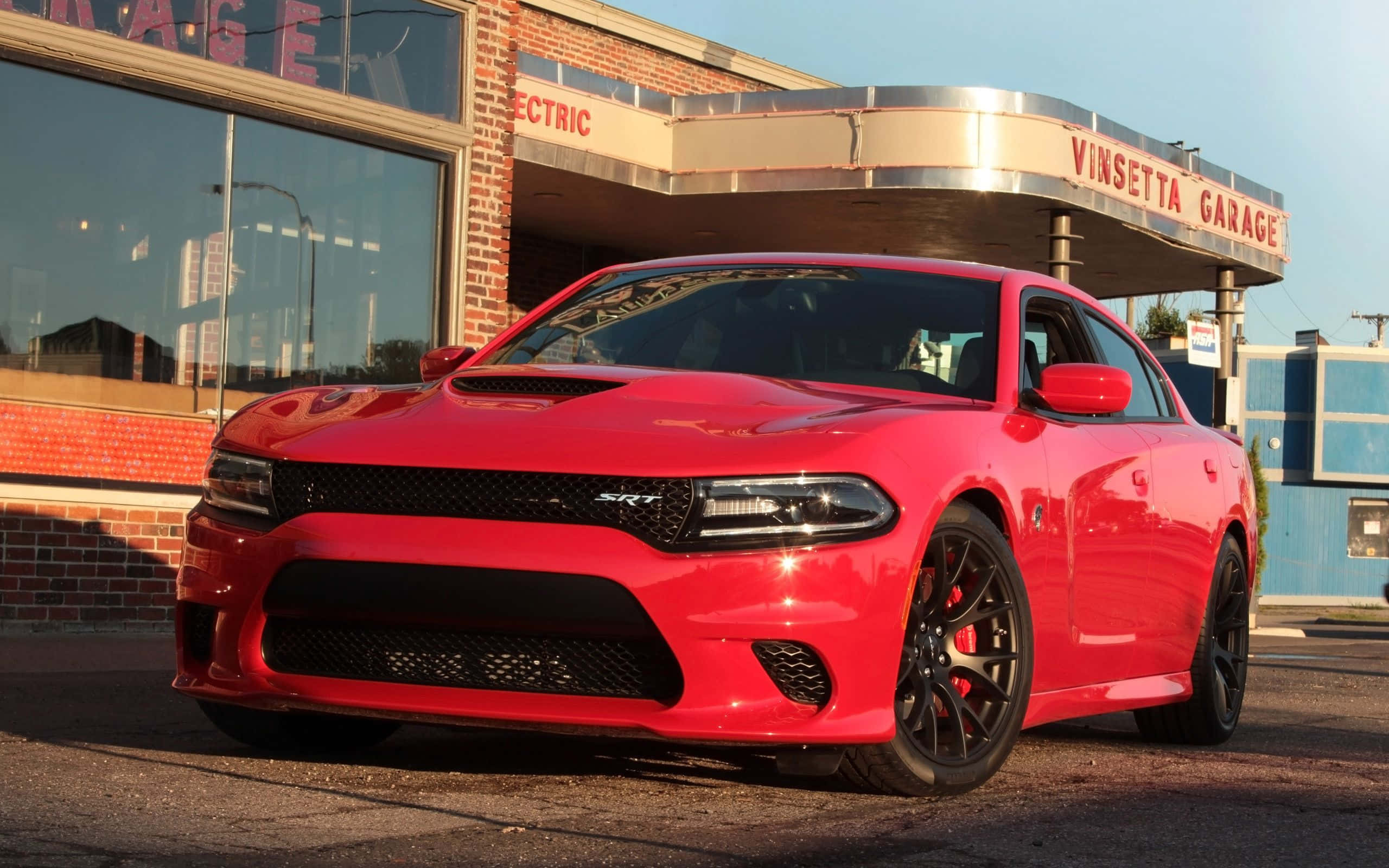 Dodge Charger 桌布 壁紙 — 一輛光亮的紅色Dodge Charger SRT停在復古磚造車庫前，背景是晴朗的藍天。