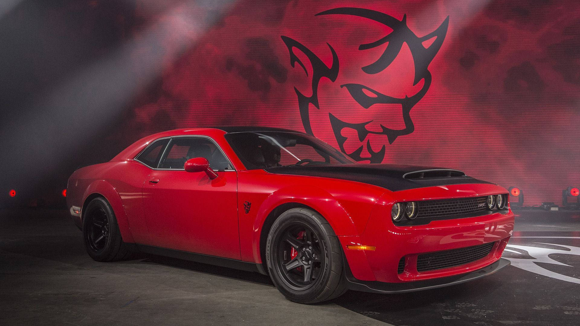 Challenger 桌布 壁紙 — 一輛光亮的紅色Dodge Challenger Hellcat，帶有黑色引擎蓋和車輪，在戲劇性的紅色燈光下，以魔鬼標誌背景展示。
