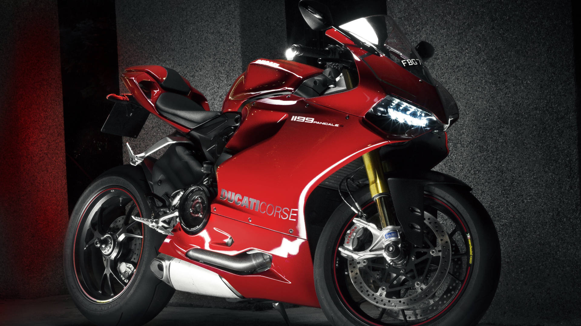杜卡迪 桌布 壁紙 — 一輛光亮的紅色Ducati 1199 Panigale摩托車在攝影棚燈光下，以深色紋理牆壁為背景閃閃發光。