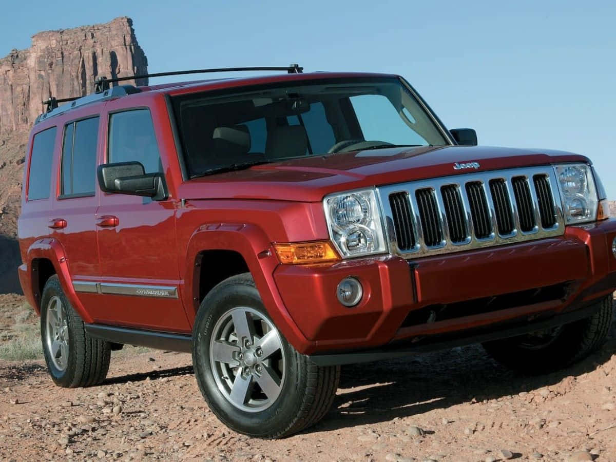 Jeep Commander 桌布 壁紙 — 一輛光亮的紅色Jeep Wrangler在崎嶇的沙漠地形上蓄勢待發，背景是聳立的岩石構造，天空清澈湛藍。