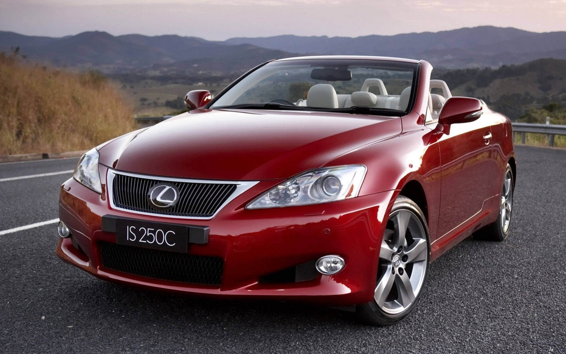 Lexus 桌布 壁紙 — 一輛光亮的紅色Lexus IS 250C敞篷車停泊在日落時分蜿蜒的山路上，背景有山丘。