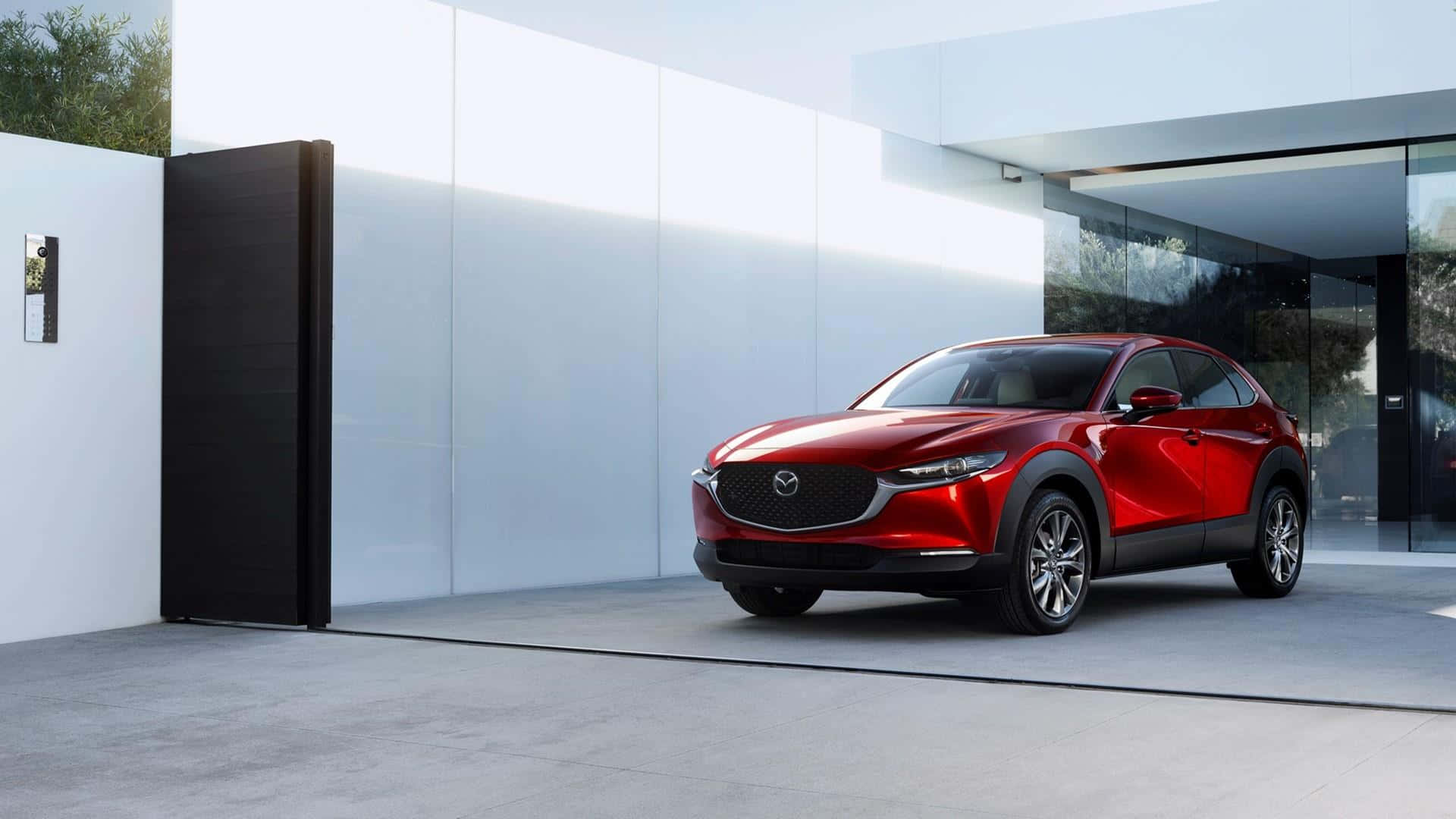 Mazda Cx-30 桌布 壁紙 — 一輛光亮的紅色Mazda CX-30 SUV停在一棟帶玻璃門和黑色大門的現代白色房屋前。