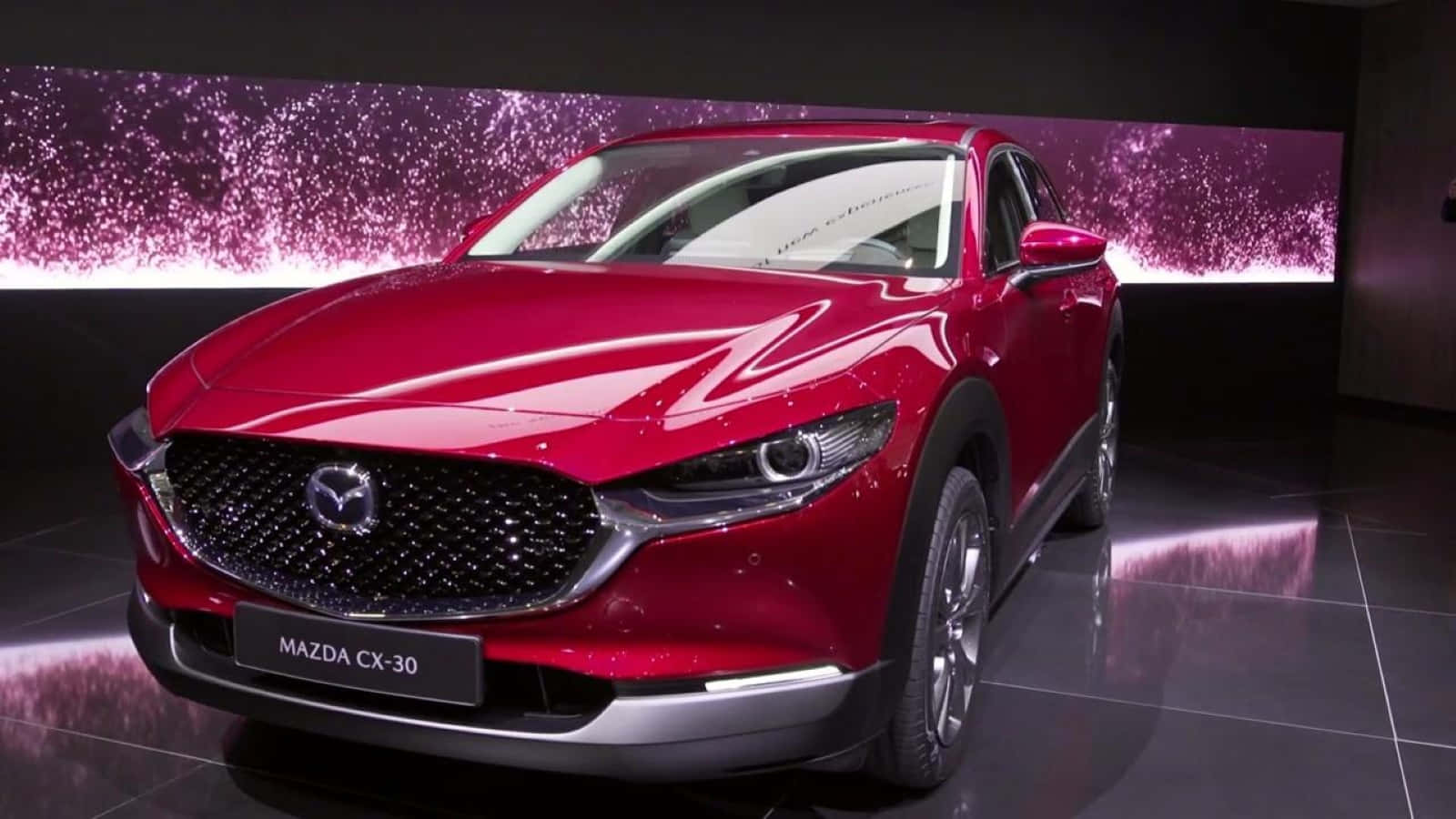 Mazda Cx-30 桌布 壁紙 — 一輛光亮的紅色Mazda CX-30 SUV在攝影棚燈光下，在反光地板上閃爍著紫色閃爍的背景。