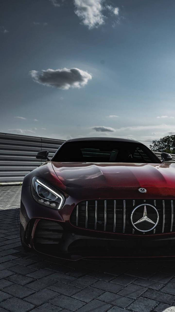R 桌布 壁紙 — 一輛光亮的紅色Mercedes-AMG GT跑車停泊在鵝卵石路面上，天空部分多雲。