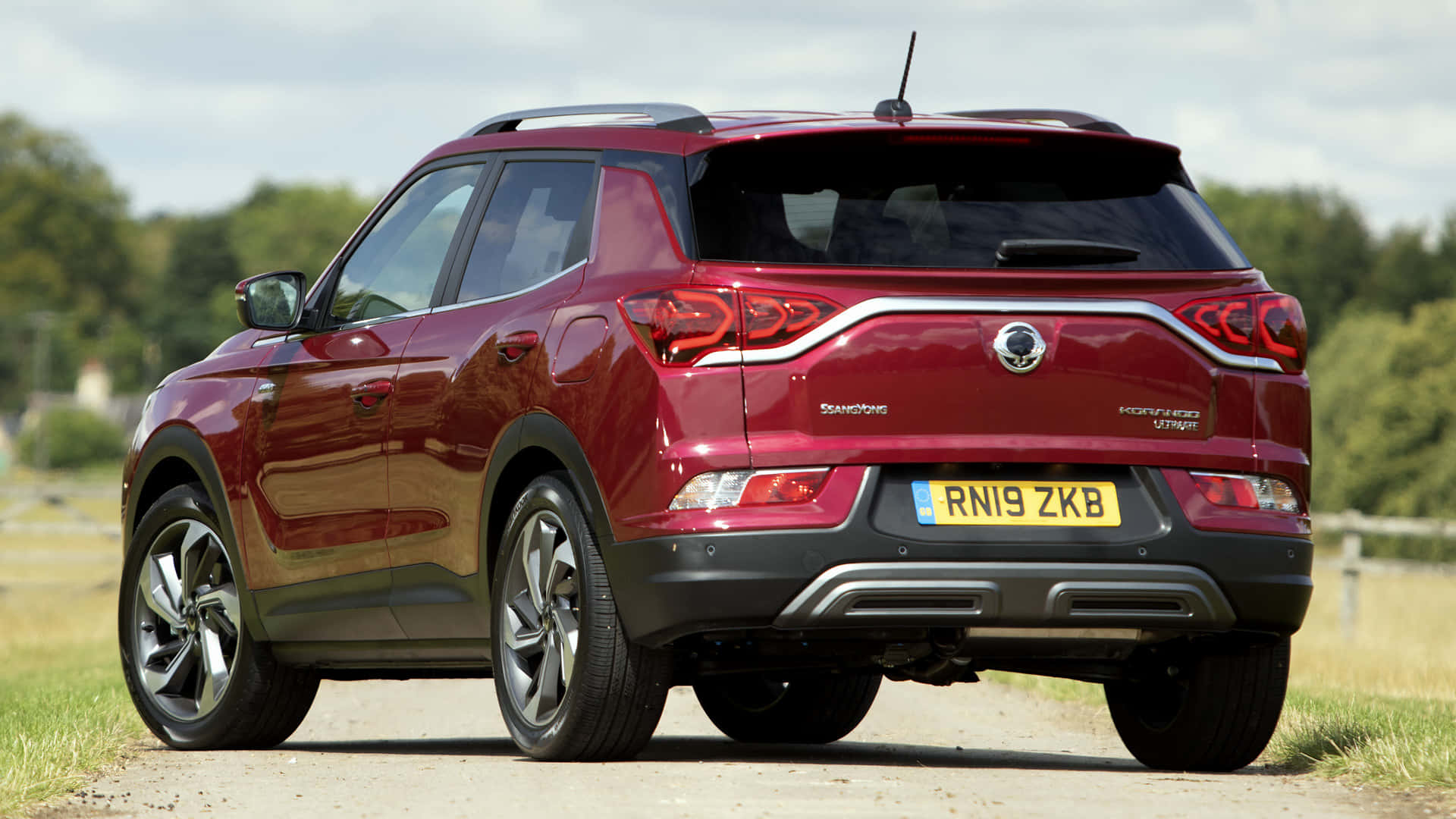 Ssangyong 桌布 壁紙 — 一輛光亮的紅色SsangYong Tivoli SUV停泊在碎石路上，背景是綠樹和陰天。