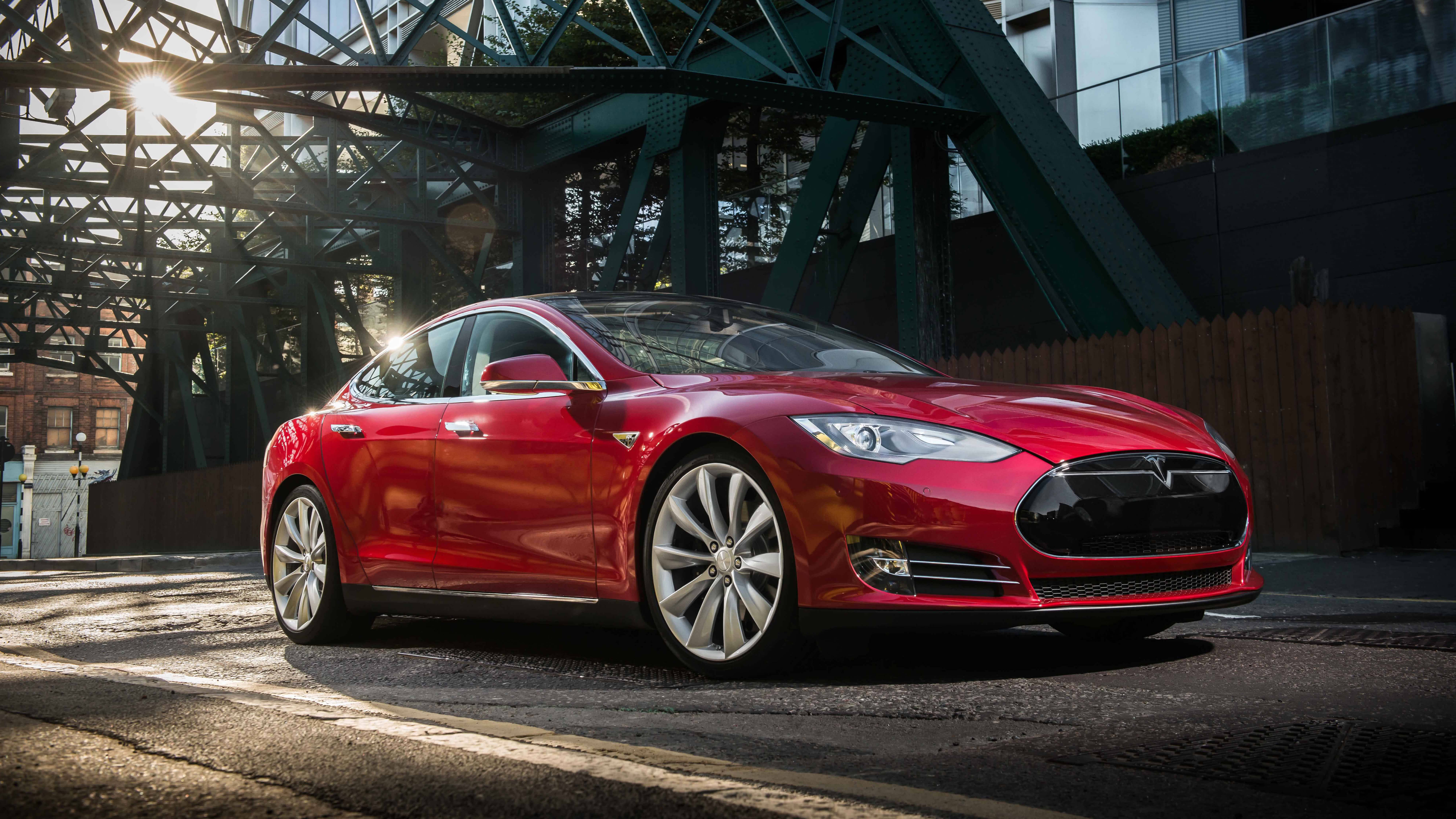 特斯拉 桌布 壁紙 — 一輛光亮的紅色Tesla Model S停放在綠色鋼橋下，陽光穿過桁架照射進來。