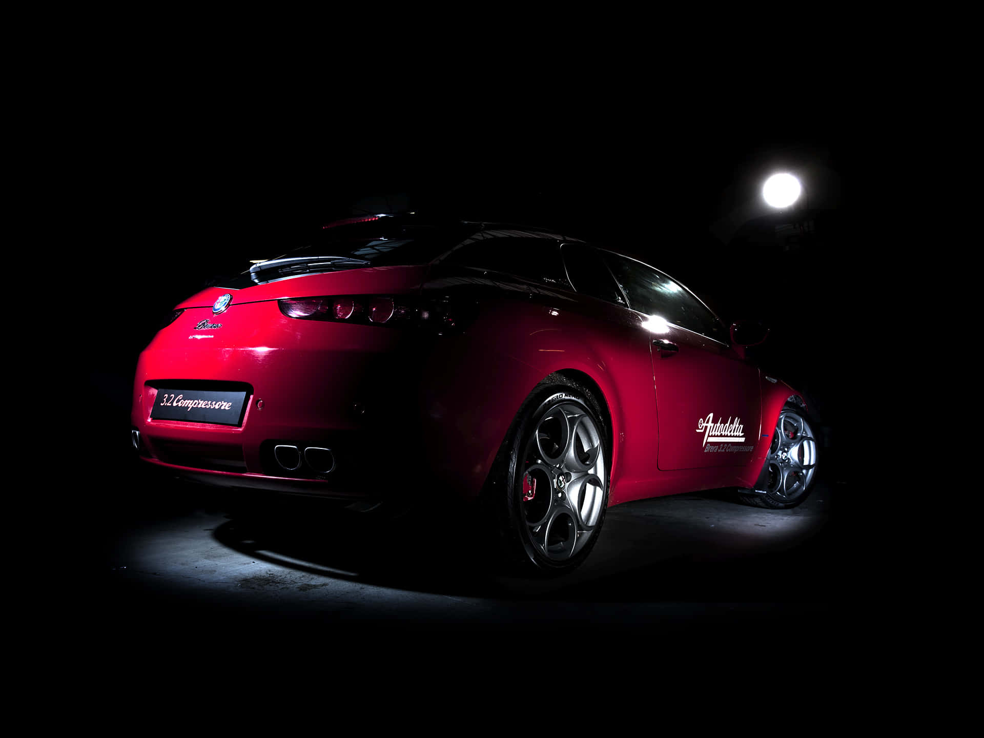 Alfa Romeo Brera 桌布 壁紙 — 一輛光亮的紅色愛快羅密歐跑車在漆黑背景中由單一聚光燈戲劇性地照亮。