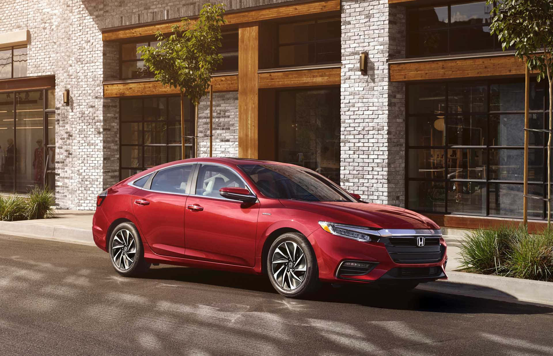 Honda Insight 桌布 壁紙 — 一輛光亮的紅色本田轎車停放在陽光普照的街道上，旁邊是一座現代磚木建築。