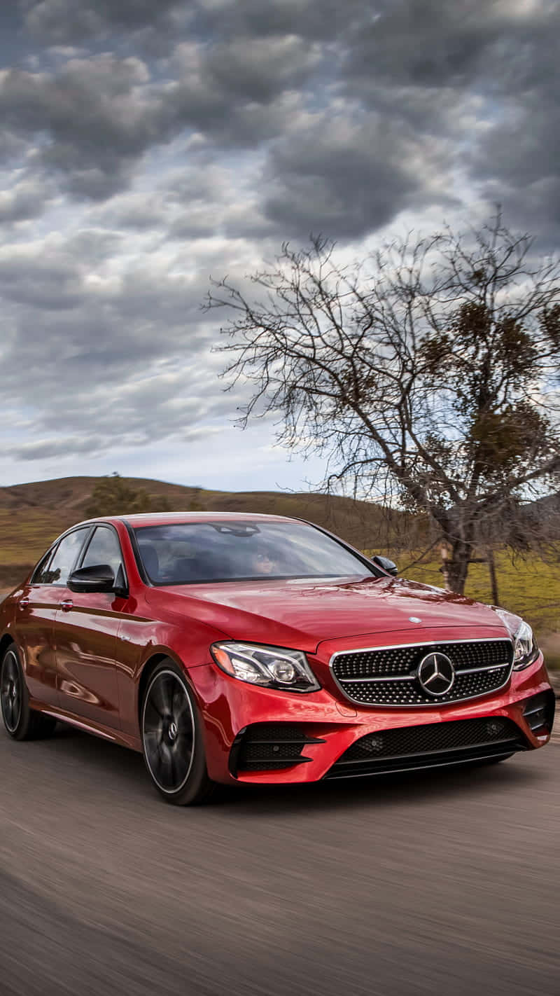 Red Car 桌布 壁紙 — 一輛光亮的紅色梅賽德斯轎車在戲劇性的多雲天空下，沿著鄉村道路疾馳，背景是光禿禿的樹木。