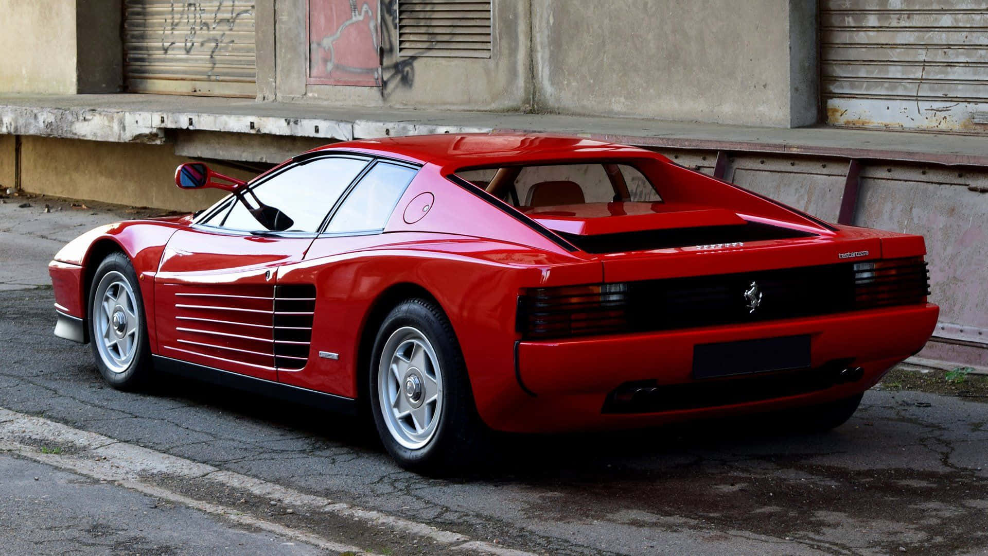 Ferrari Testarossa 桌布 壁紙 — 一輛光亮的紅色法拉利Testarossa停放在佈滿裂縫的城市街道上，旁邊是帶有塗鴉的風化混凝土牆。