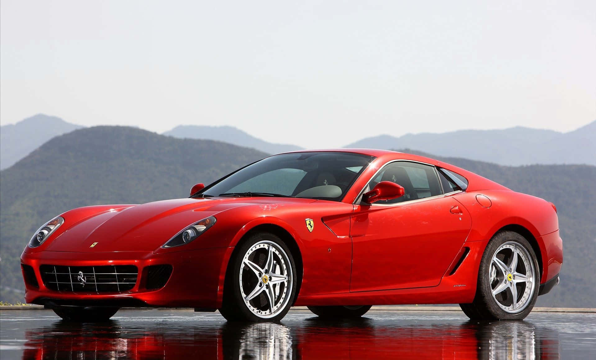 Ferrari 599 Gtb Fiorano 桌布 壁紙 — 一輛光亮的紅色法拉利跑車在明亮的日光下，在濕滑的道路上閃閃發光，背景是山巒。