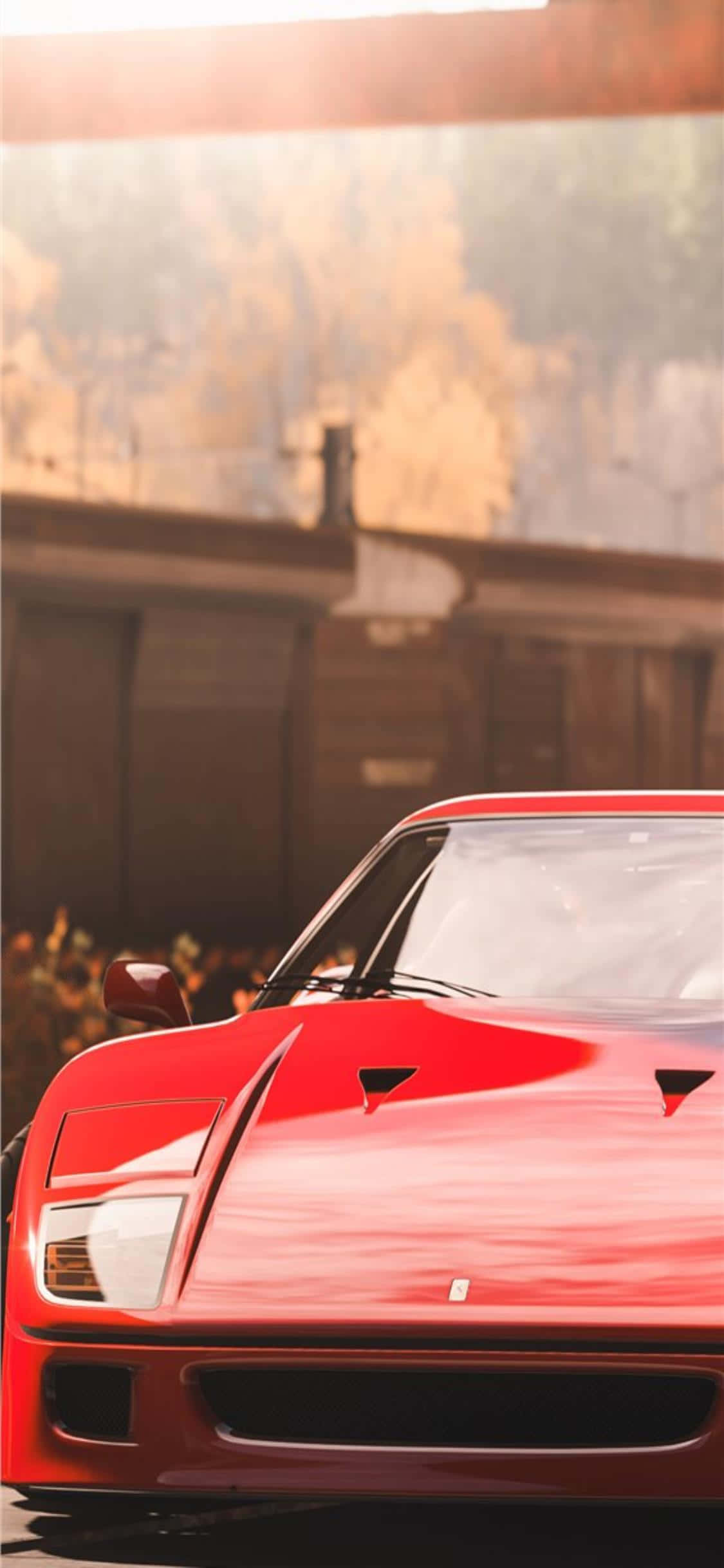 iPhone Xs Forza Horizon 4 桌布 壁紙 — 一輛光亮的紅色法拉利跑車在溫暖的金色陽光下閃耀，背景是模糊的鄉村建築。