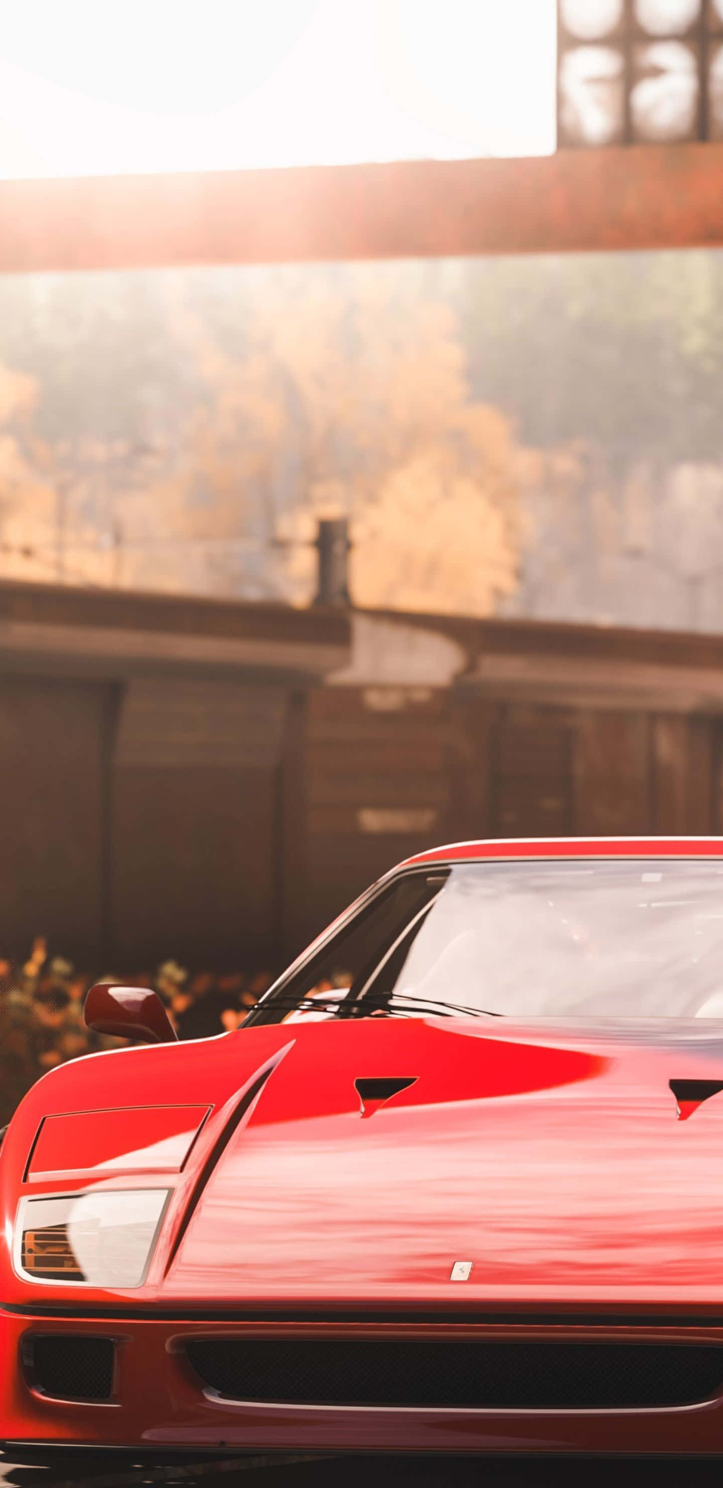 Pixel 3xl Forza Horizon 4 桌布 壁紙 — 一輛光亮的紅色法拉利跑車在溫暖的金色陽光下閃耀，背景是模糊的工業建築和秋天的樹木。