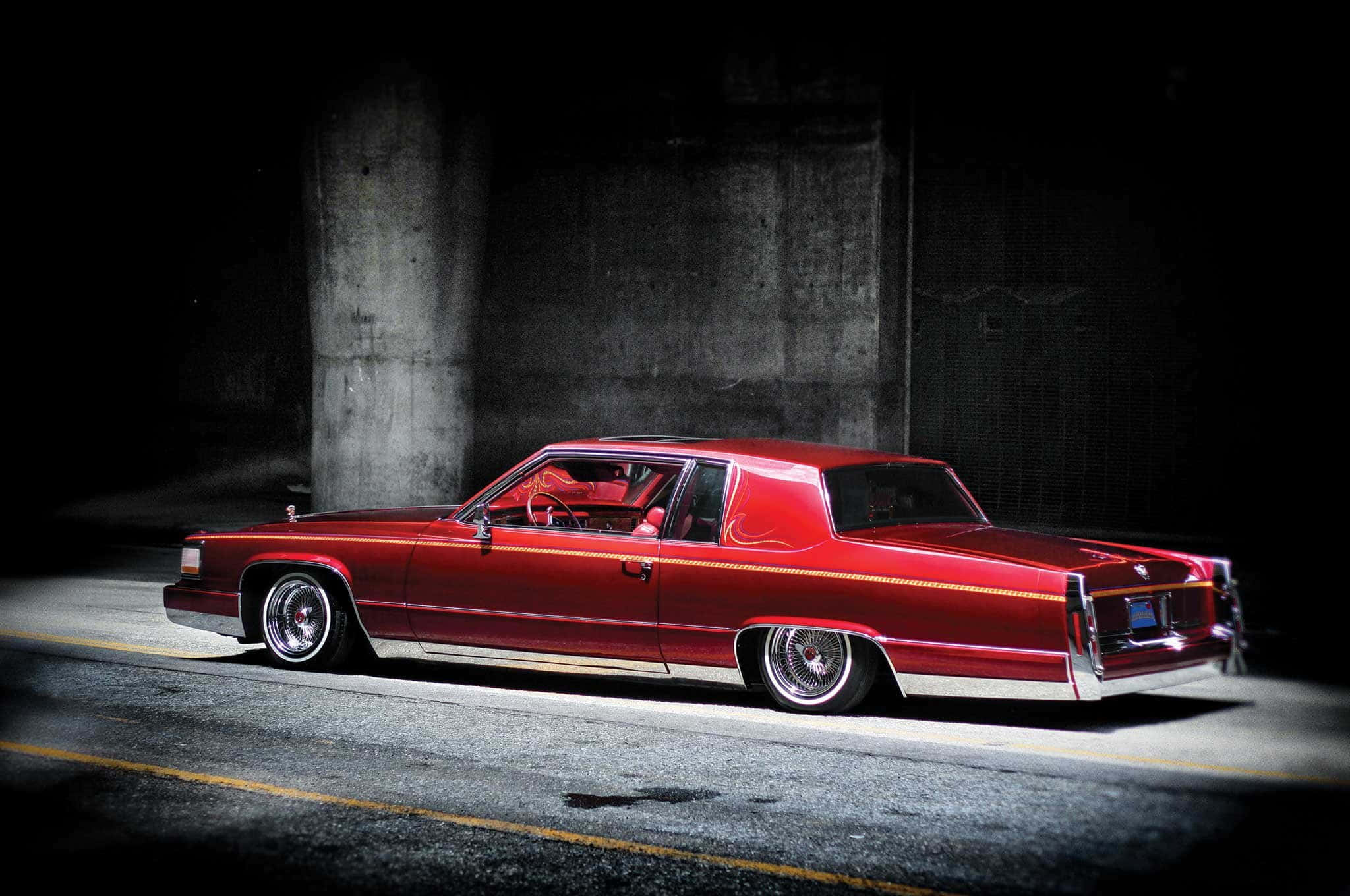 Cadillac Deville 桌布 壁紙 — 一輛光亮的紅色經典汽車配備訂製輪圈，在夜晚的混凝土天橋下被戲劇性地照亮。
