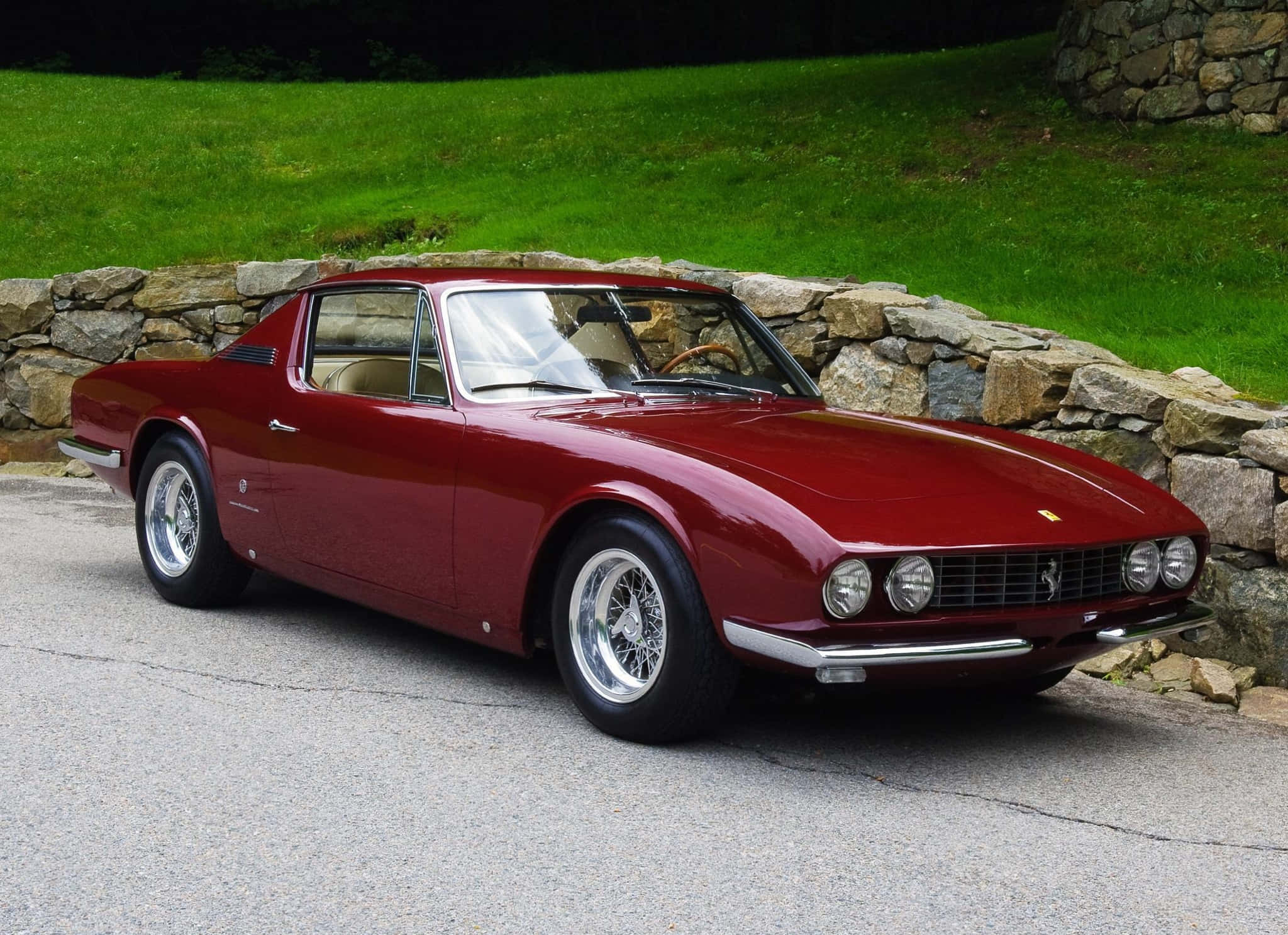 Vintage Ferrari 桌布 壁紙 — 一輛光亮的紅色經典法拉利跑車停放在石牆和綠草旁邊的鋪砌道路上。