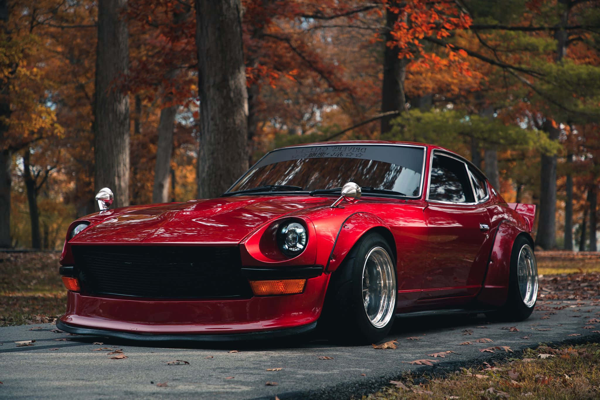 Datsun 桌布 壁紙 — 一輛光亮的紅色經典跑車停放在落葉滿佈的森林道路上，秋樹環繞。