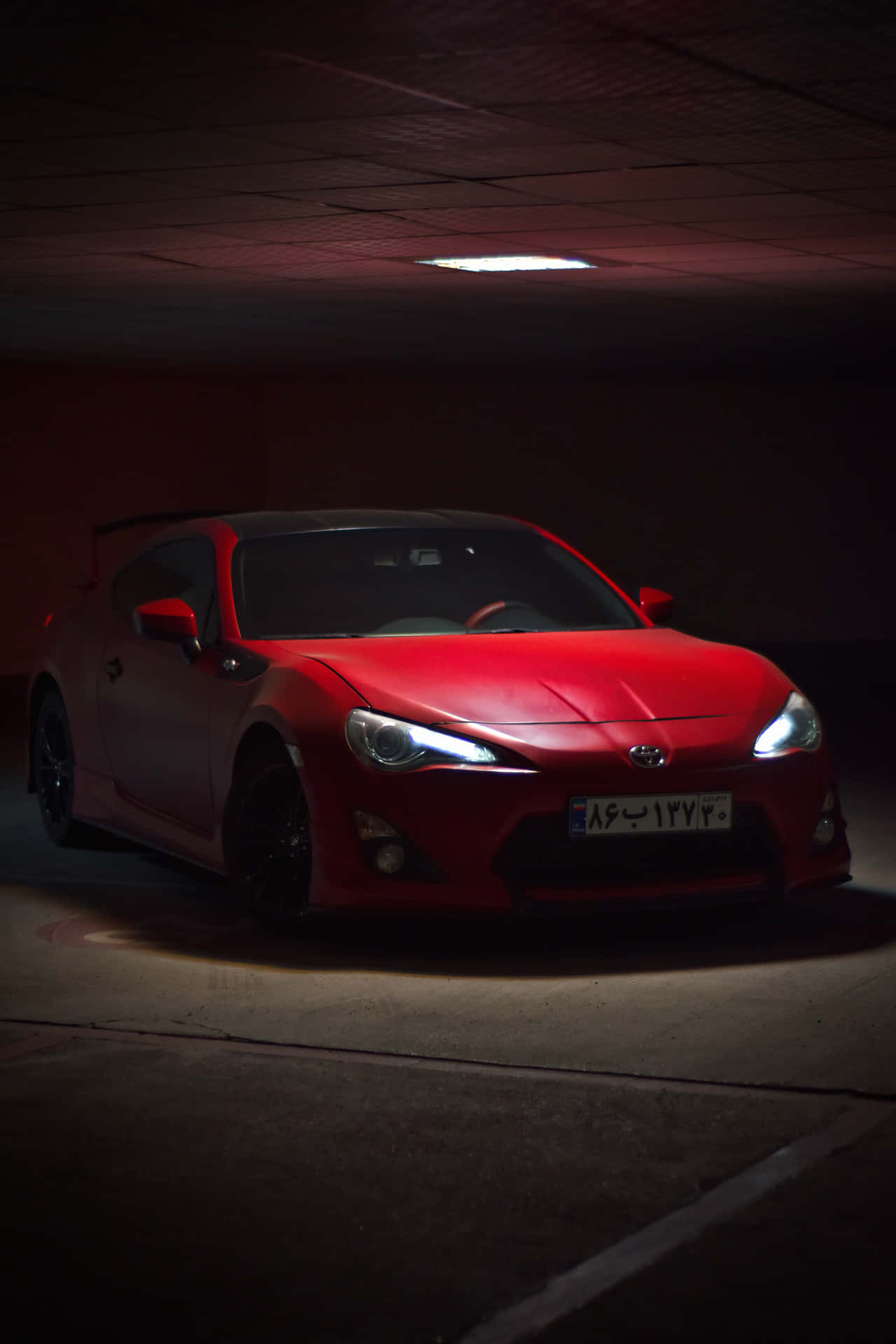 紅色跑車停放在光線昏暗的地下車庫，頭頂有一盞燈。 — Toyota Supra Mk4 壁紙