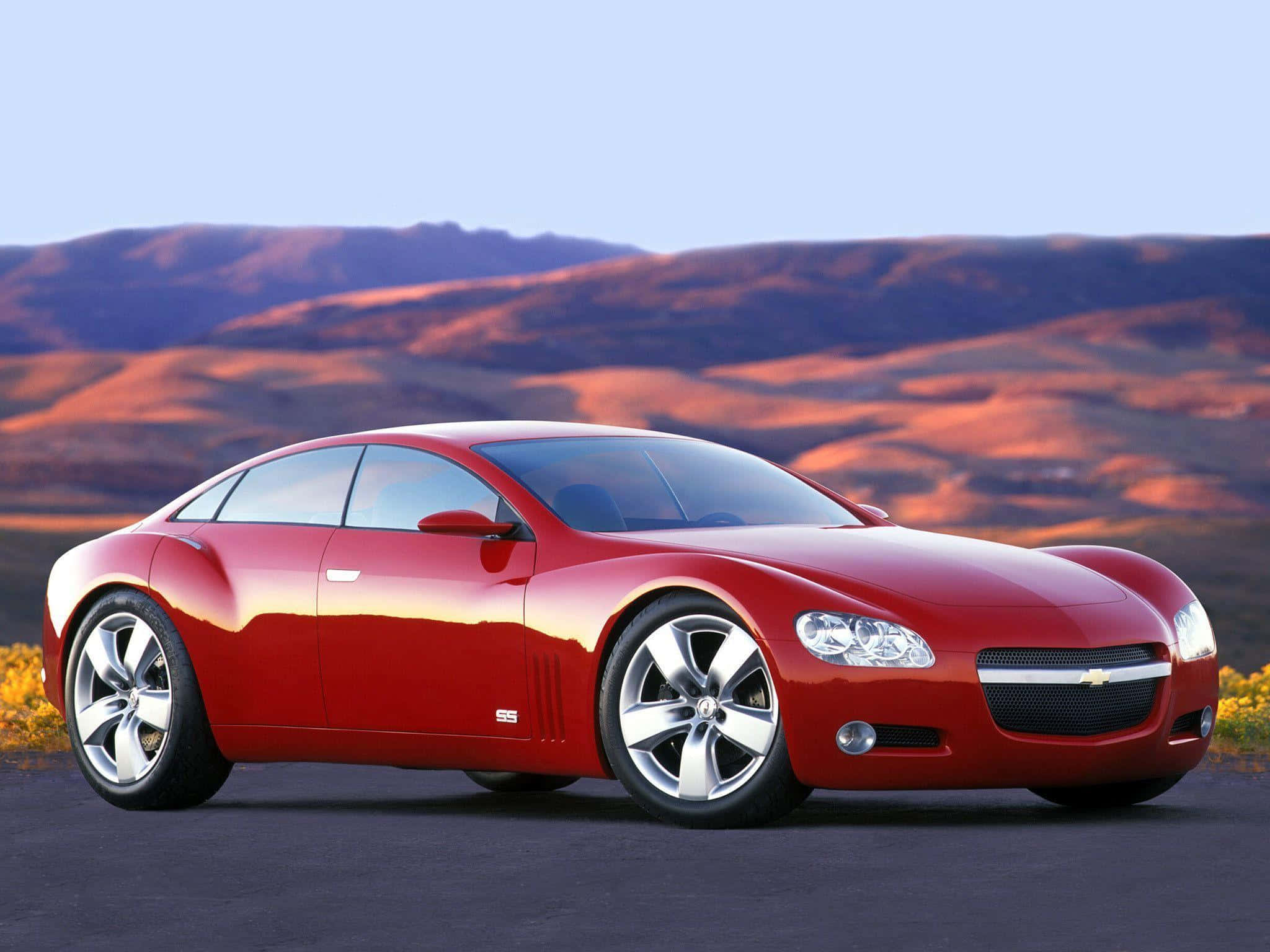 chevy 桌布 壁紙 — 一輛光亮的紅色雪佛蘭概念車在金色夕陽下，在連綿起伏的沙漠山丘映襯下閃閃發光。