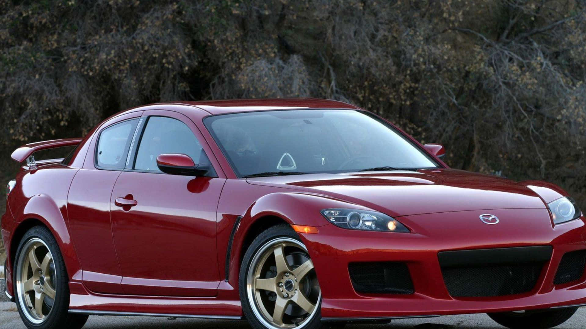 Mazda Rx-8 桌布 壁紙 — 一輛光亮的紅色馬自達RX-8跑車配金色輪圈，停泊在柏油路上，背景是乾枯的樹木。
