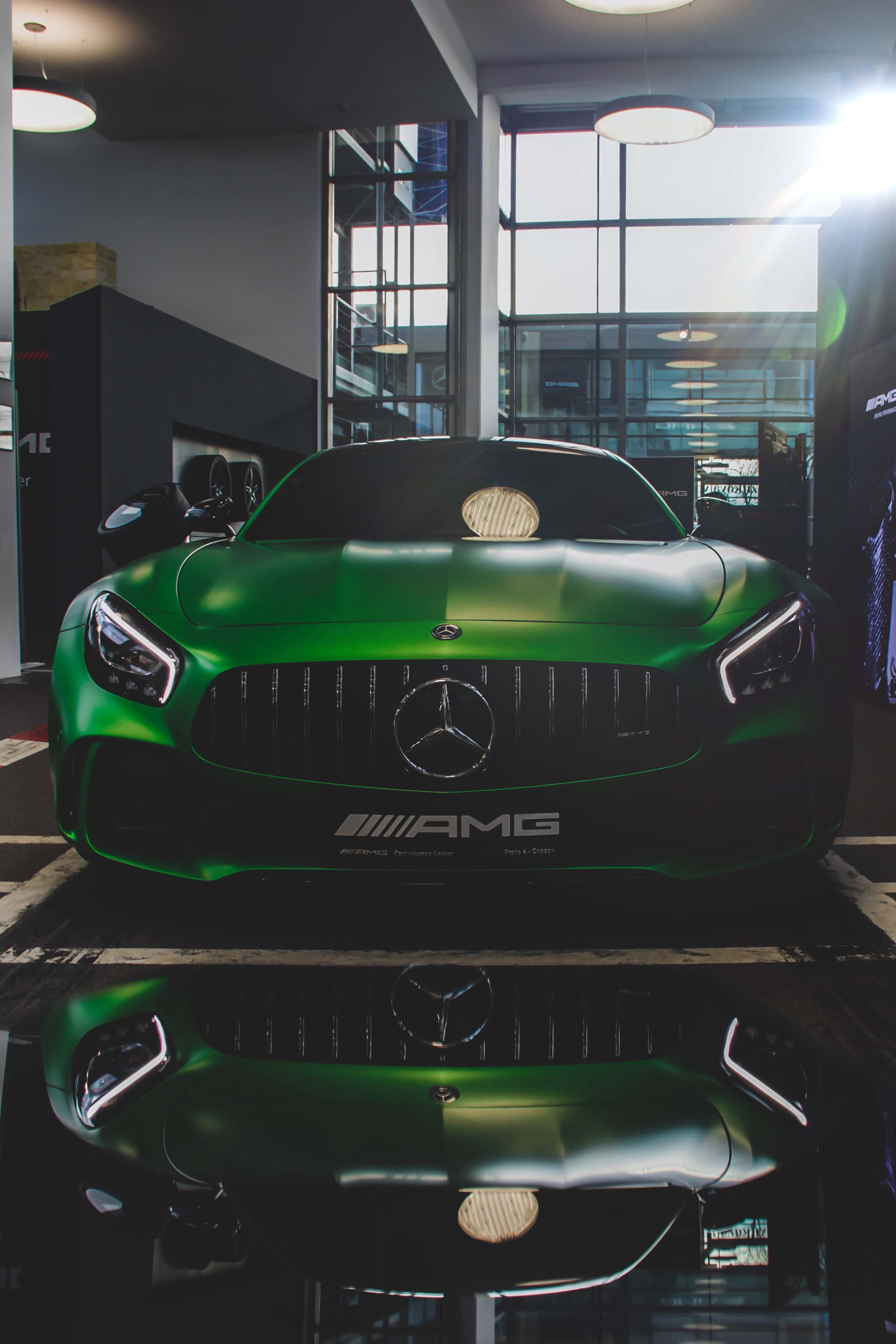 房屋 桌布 壁紙 — 一輛光亮的綠色Mercedes-AMG跑車在明亮的展廳燈光下閃閃發光，其倒影映照在地板上。