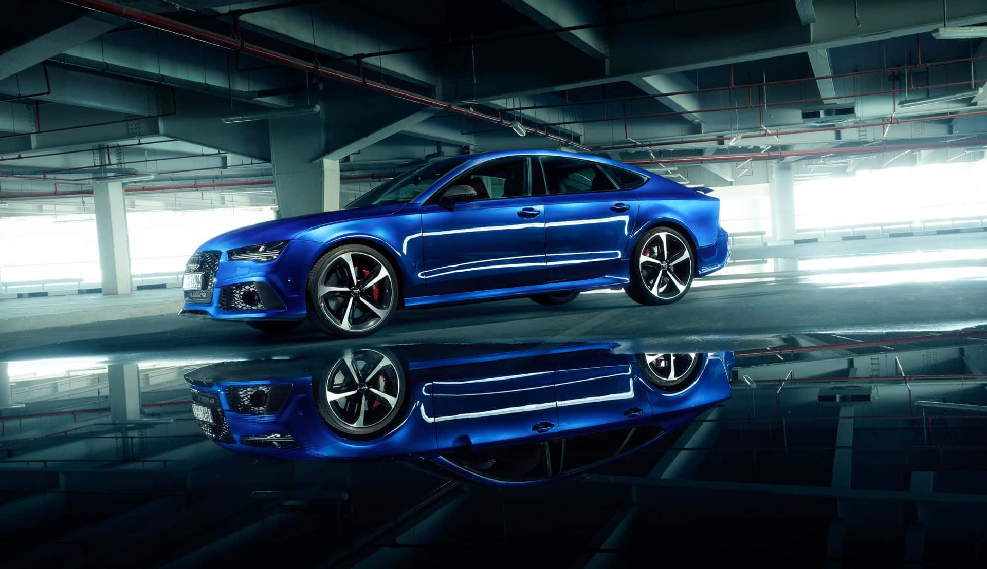 Audi S7 桌布 壁紙 — 一輛光亮的藍色跑車在工業照明下閃閃發光，在地下停車場的濕漉漉路面上完美倒映。