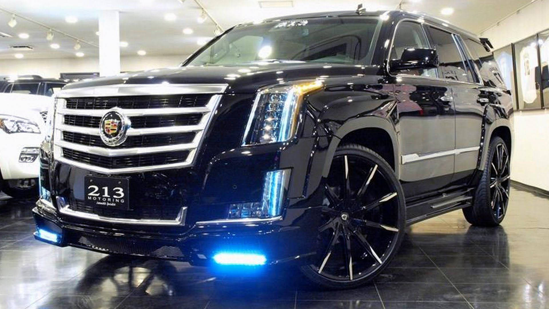 Cadillac 桌布 壁紙 — 一輛光亮的黑色 Cadillac Escalade 配備定制輪圈和藍色底盤燈，在展廳中閃閃發光。