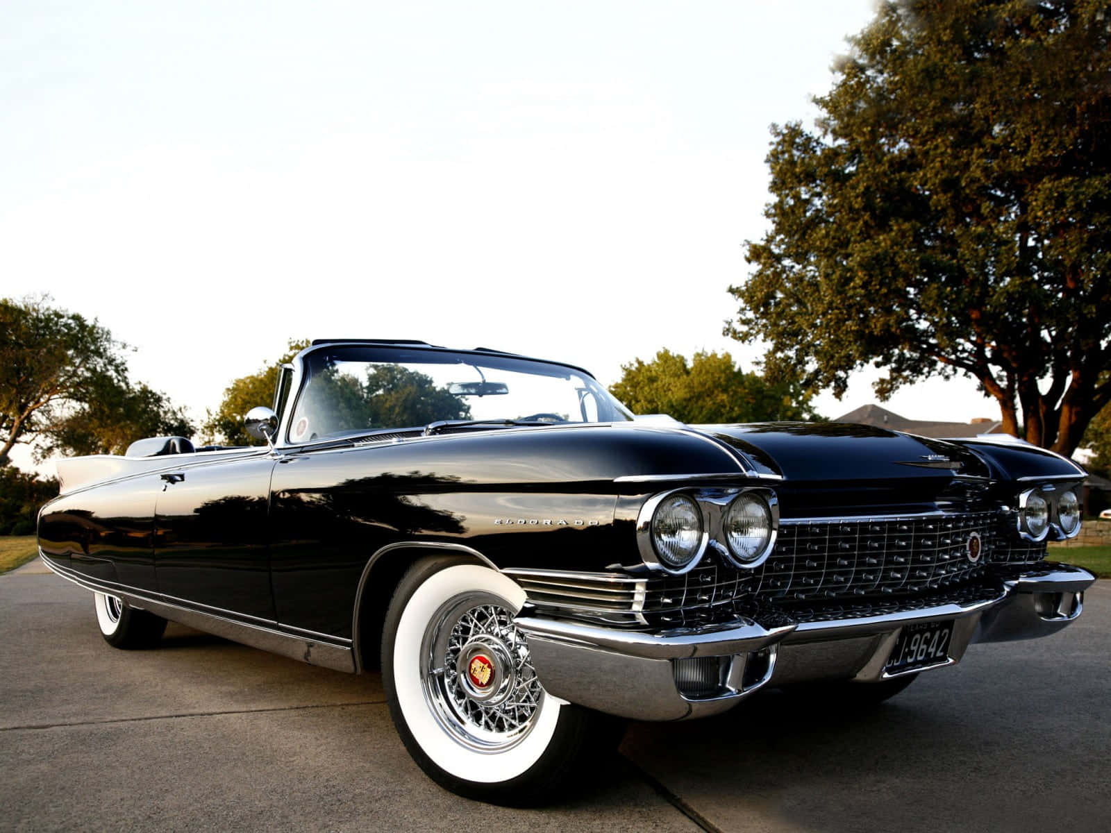 Cadillac Eldorado 桌布 壁紙 — 一輛光亮的黑色經典敞篷車配備白色輪胎，在柔和的日光下停在鋪砌的車道上閃閃發光。