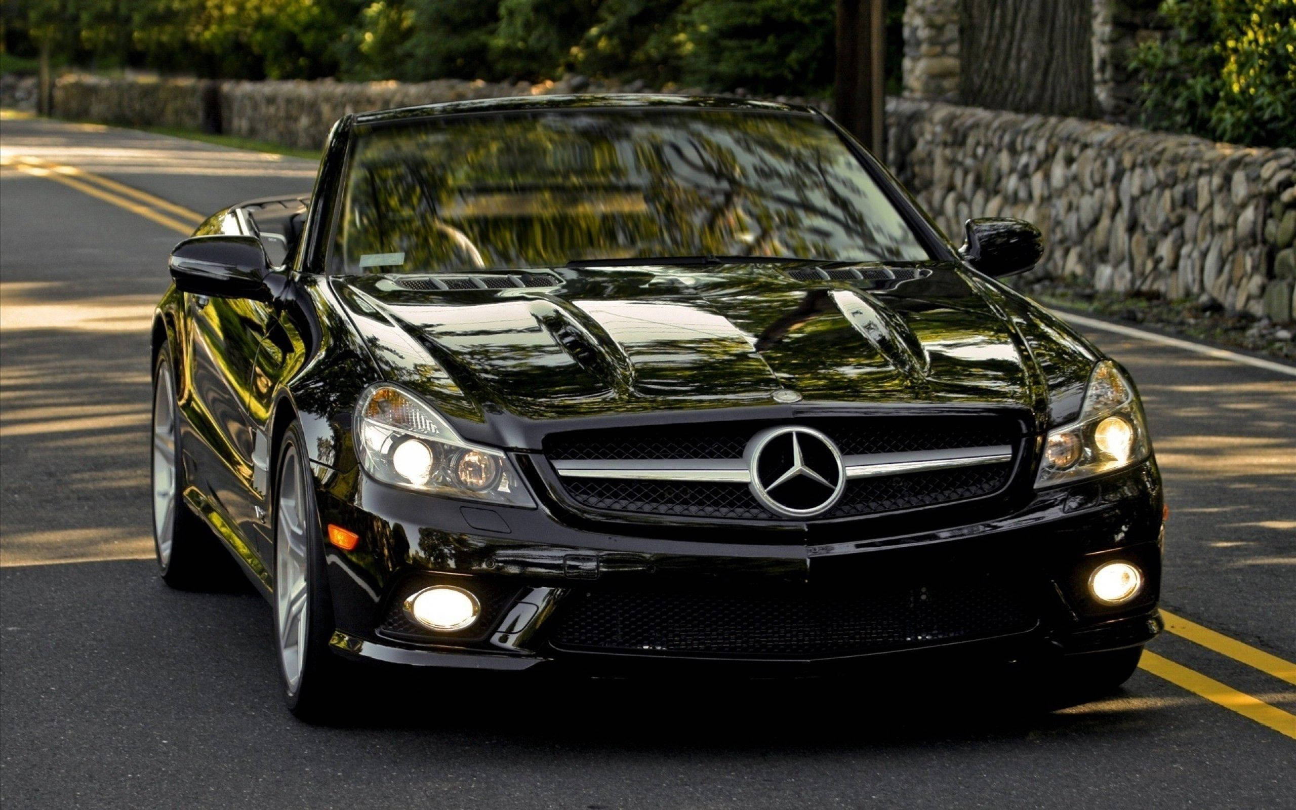 Mercedes 桌布 壁紙 — 一輛光亮的黑色賓士SLR麥拉倫敞篷車在陽光普照的樹蔭大道上閃閃發光。