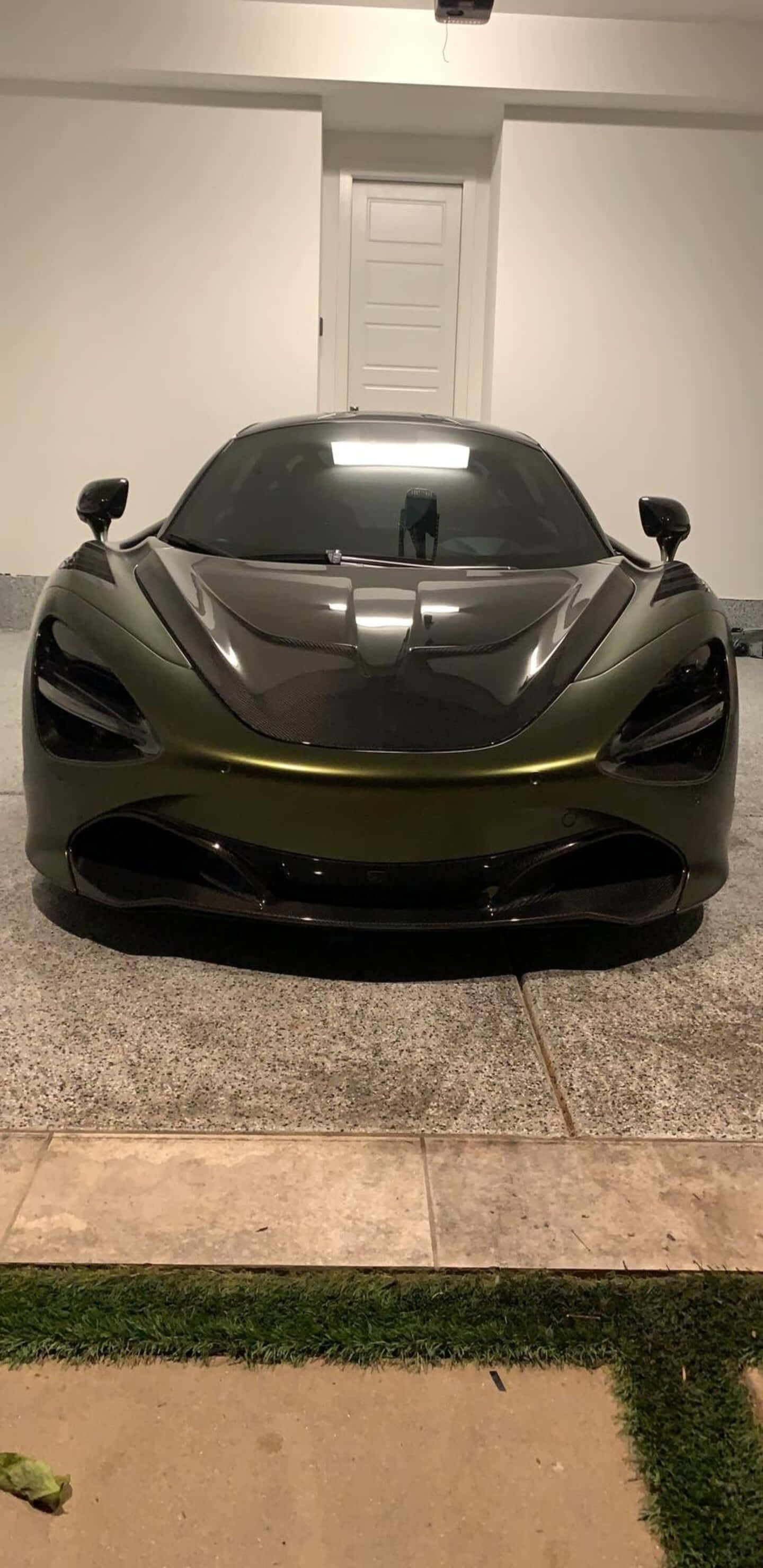 Pixel 3xl Mclaren 720s 桌布 壁紙 — 一輛光滑的啞光橄欖綠色McLaren跑車停放在室內瓷磚地板上，帶有人造草邊界。