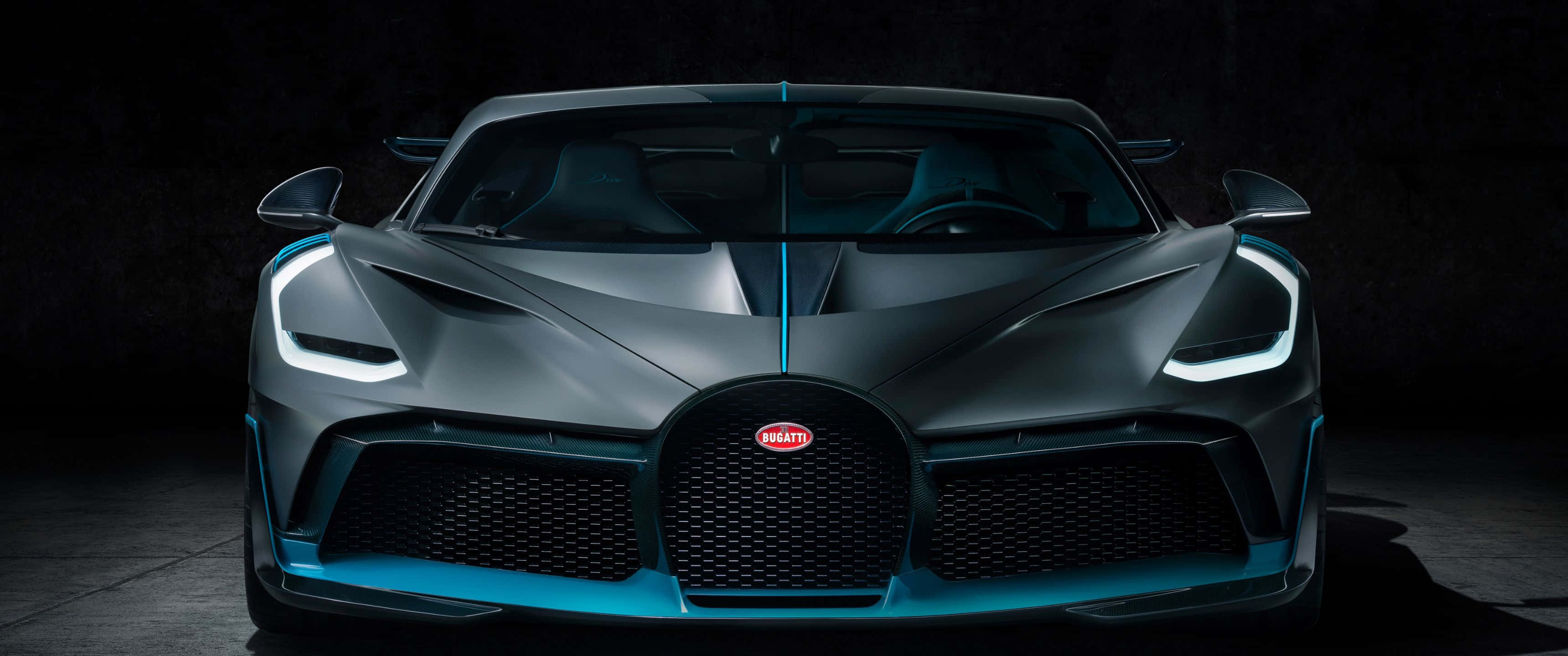 3440x1440p Bugatti 桌布 壁紙 — 一輛光滑的啞光灰色布加迪超跑，帶有發光的藍色點綴和鋒利的前燈，在黑暗的攝影棚環境中直視前方。