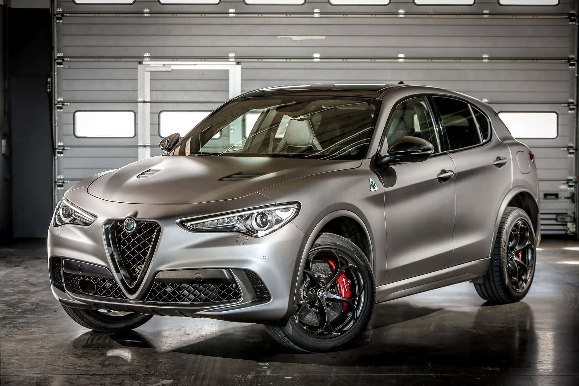 Alfa Romeo Stelvio 桌布 壁紙 — 一輛光滑的啞光銀色 Alfa Romeo SUV 配備紅色制動卡鉗，在明亮的攝影棚燈光下於現代工業車庫中展示。