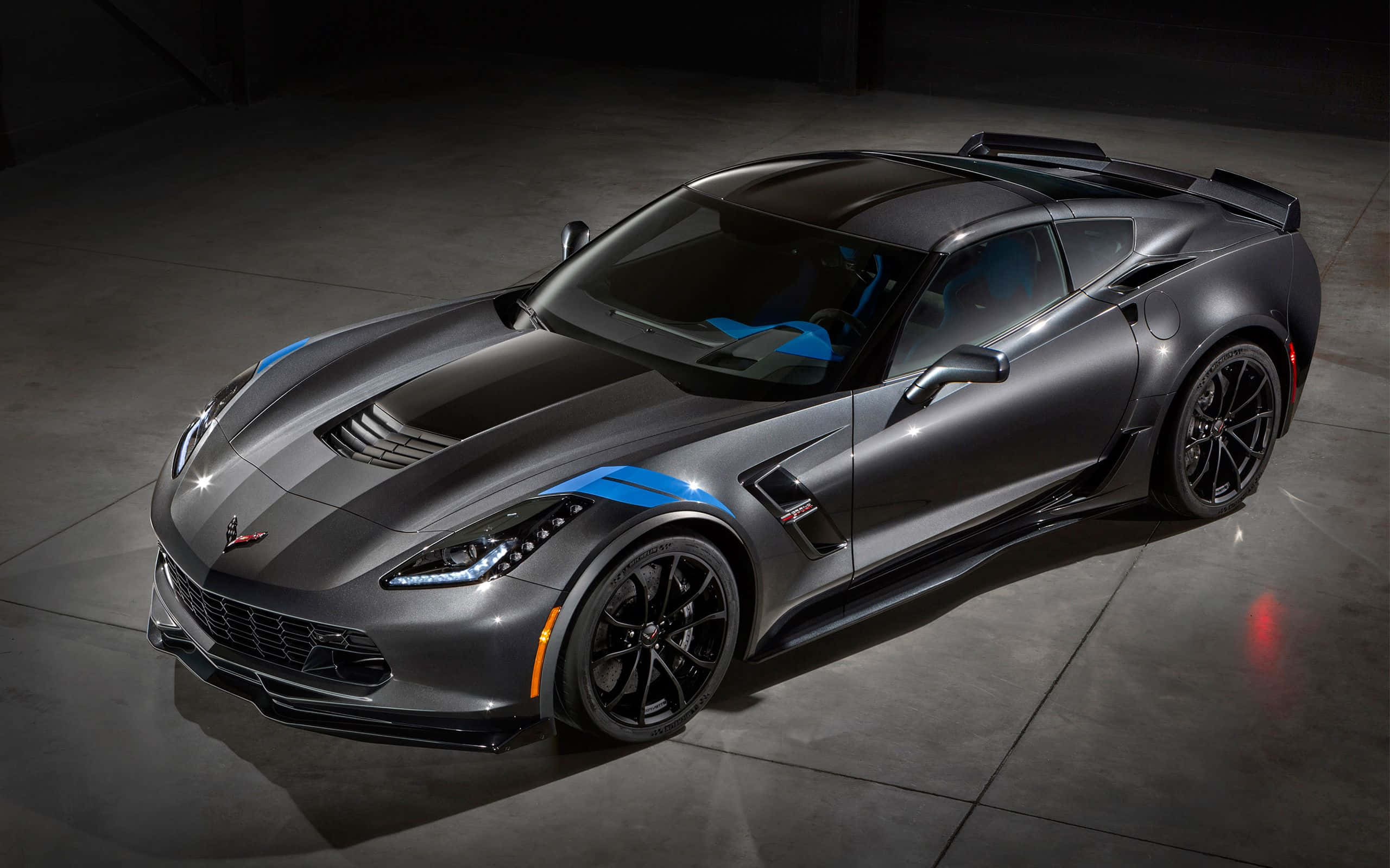 corvette 桌布 壁紙 — 一輛光滑的消光灰色Corvette跑車，帶有醒目的藍色賽車條紋，在黑暗的混凝土車庫中，在攝影棚燈光下閃閃發光。