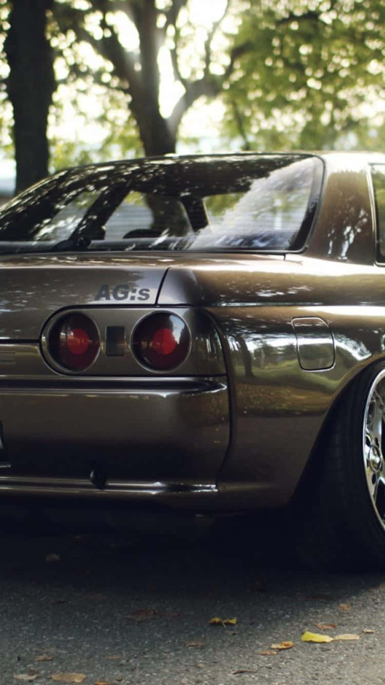 JDM 桌布 壁紙 — 一輛光滑的青銅色跑車，帶有紅色尾燈，停在秋日陽光下枝葉茂密的樹下。