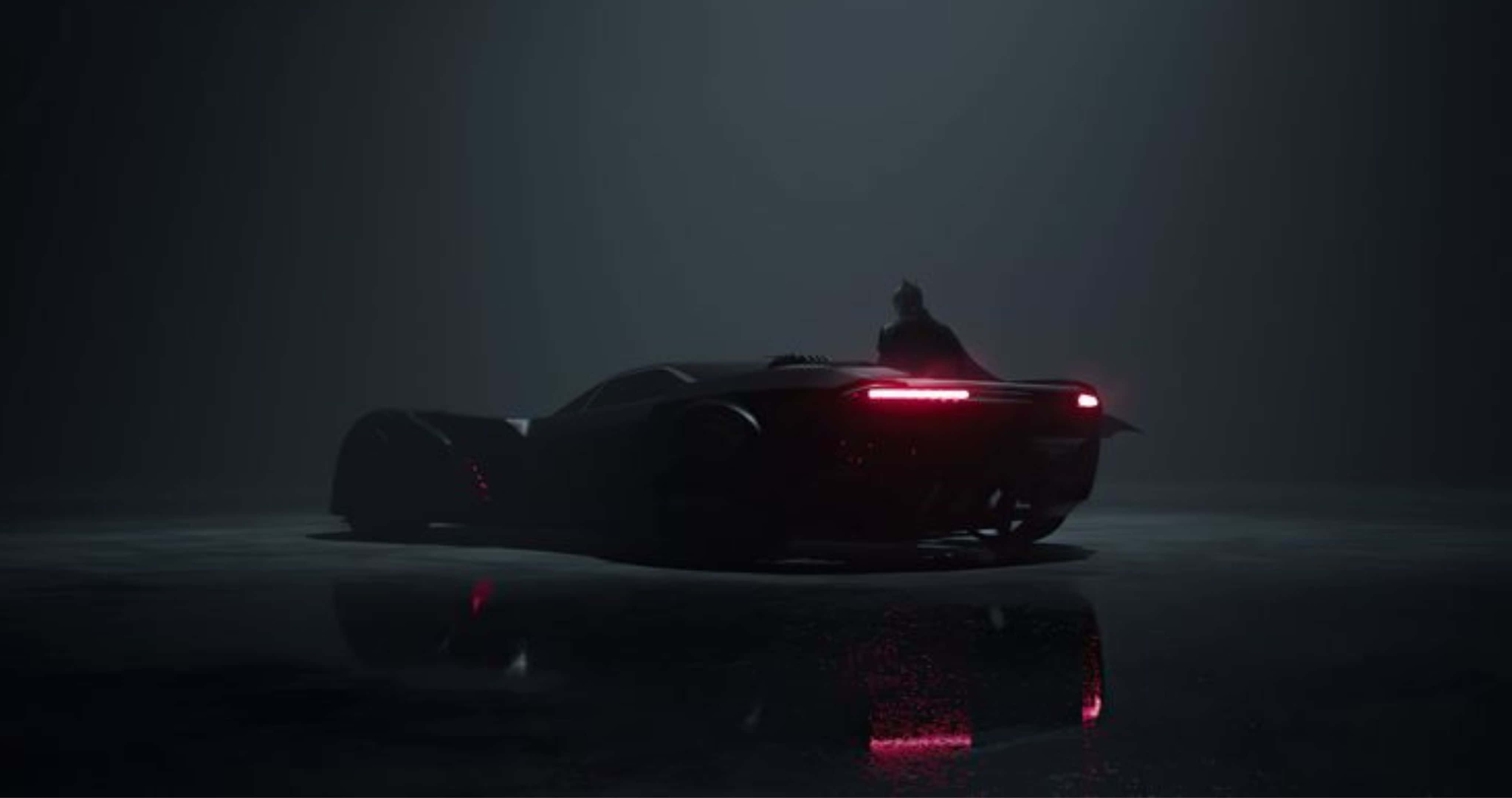 4K Batmobile 桌布 壁紙 — 一輛光滑的黑色蝙蝠車帶有發光的紅色尾燈，在潮濕的路面上反射，蝙蝠俠站在上面，處於霧濛濛的黑暗環境中。