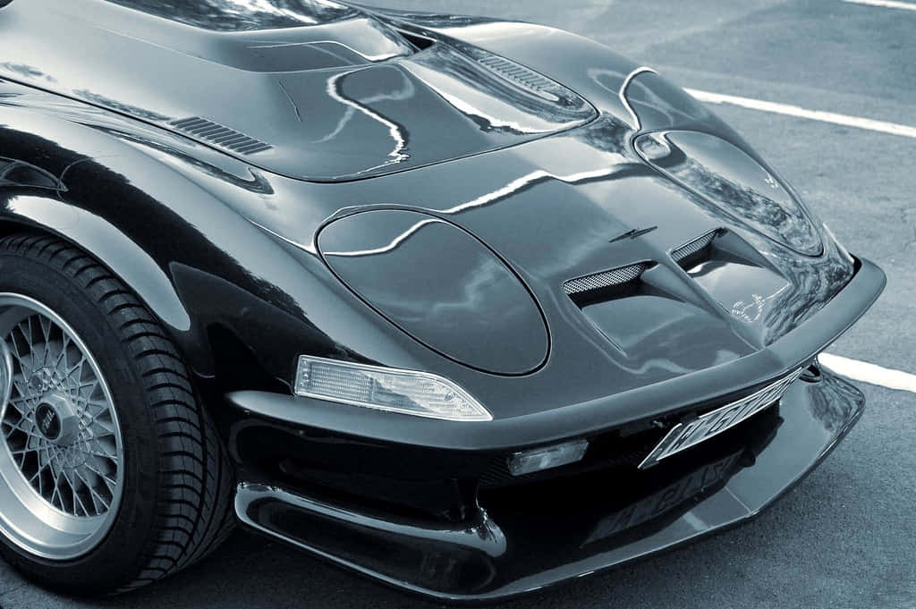 Car Hood 桌布 壁紙 — 一輛光滑的黑色跑車，帶有光澤飾面和空氣動力學曲線，停在鋪砌的路面上。