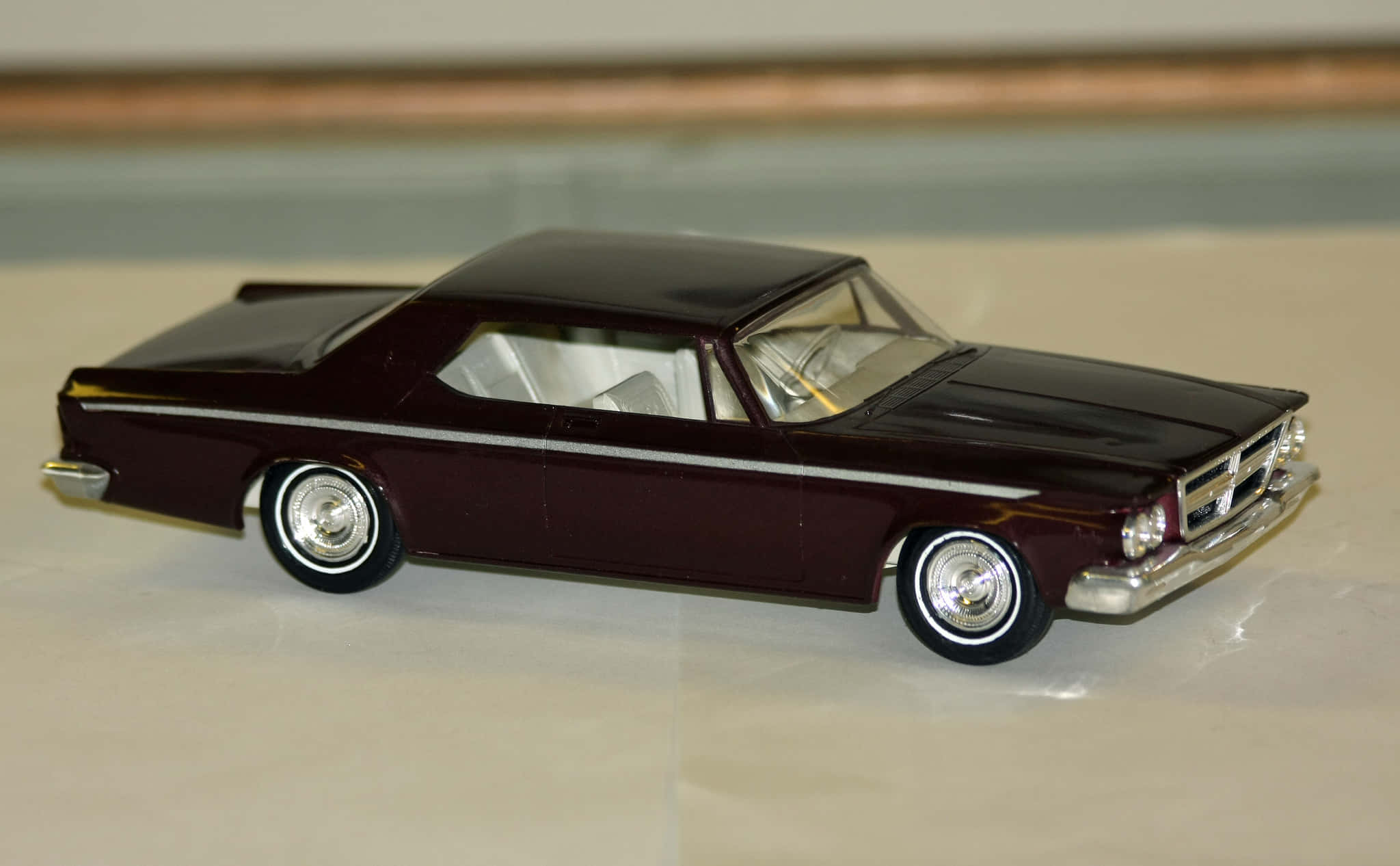 Car Model 桌布 壁紙 — 一輛光澤栗色復古車模型，帶有鍍鉻裝飾，放置在柔和室內燈光下的淺色表面上。
