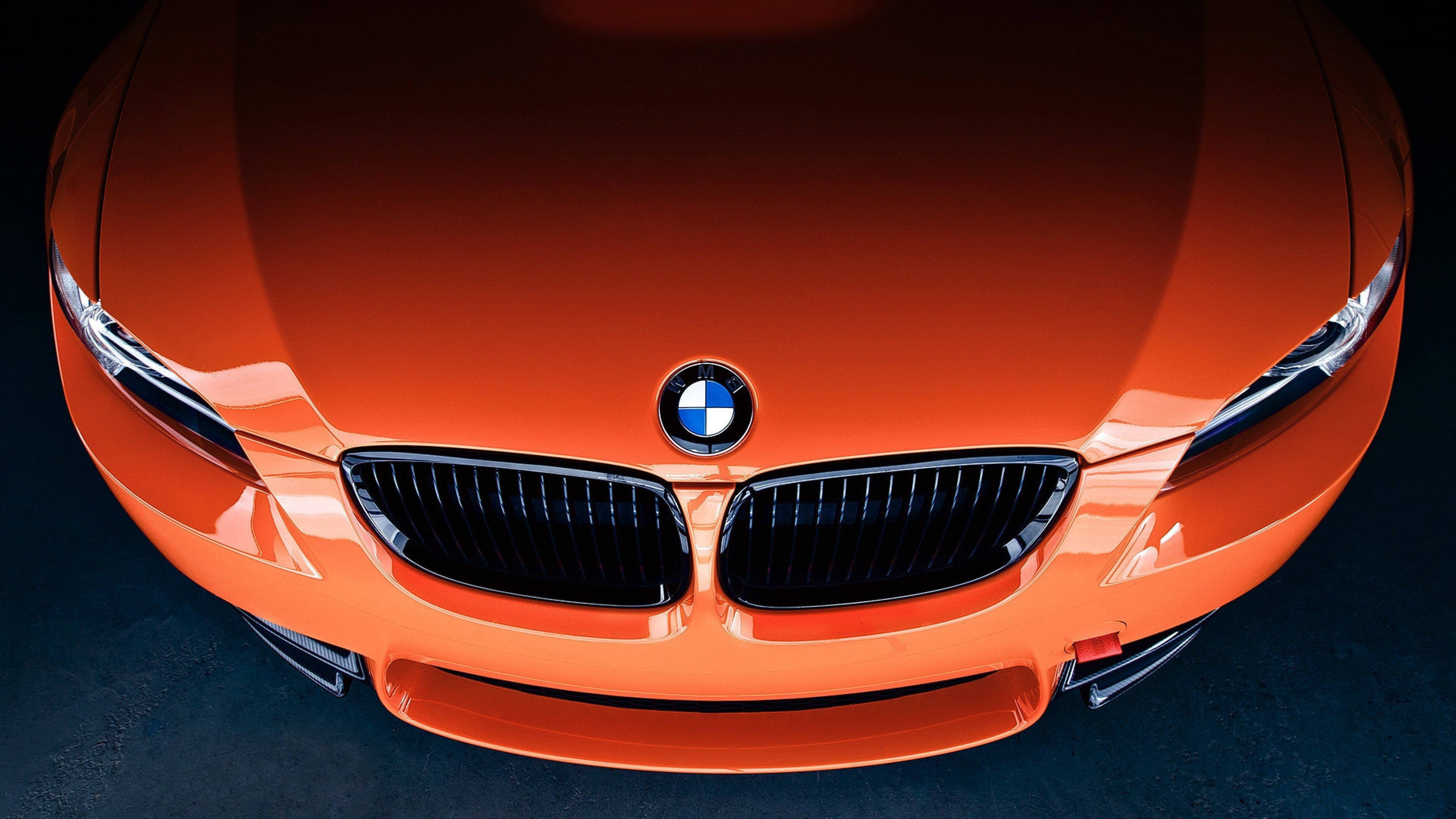 4K BMW 壁紙 桌布 壁紙 — 一輛光澤橙色寶馬汽車的前視圖，帶有標誌性的腎形格柵和鋒利的頭燈，在戲劇性的工作室燈光下。