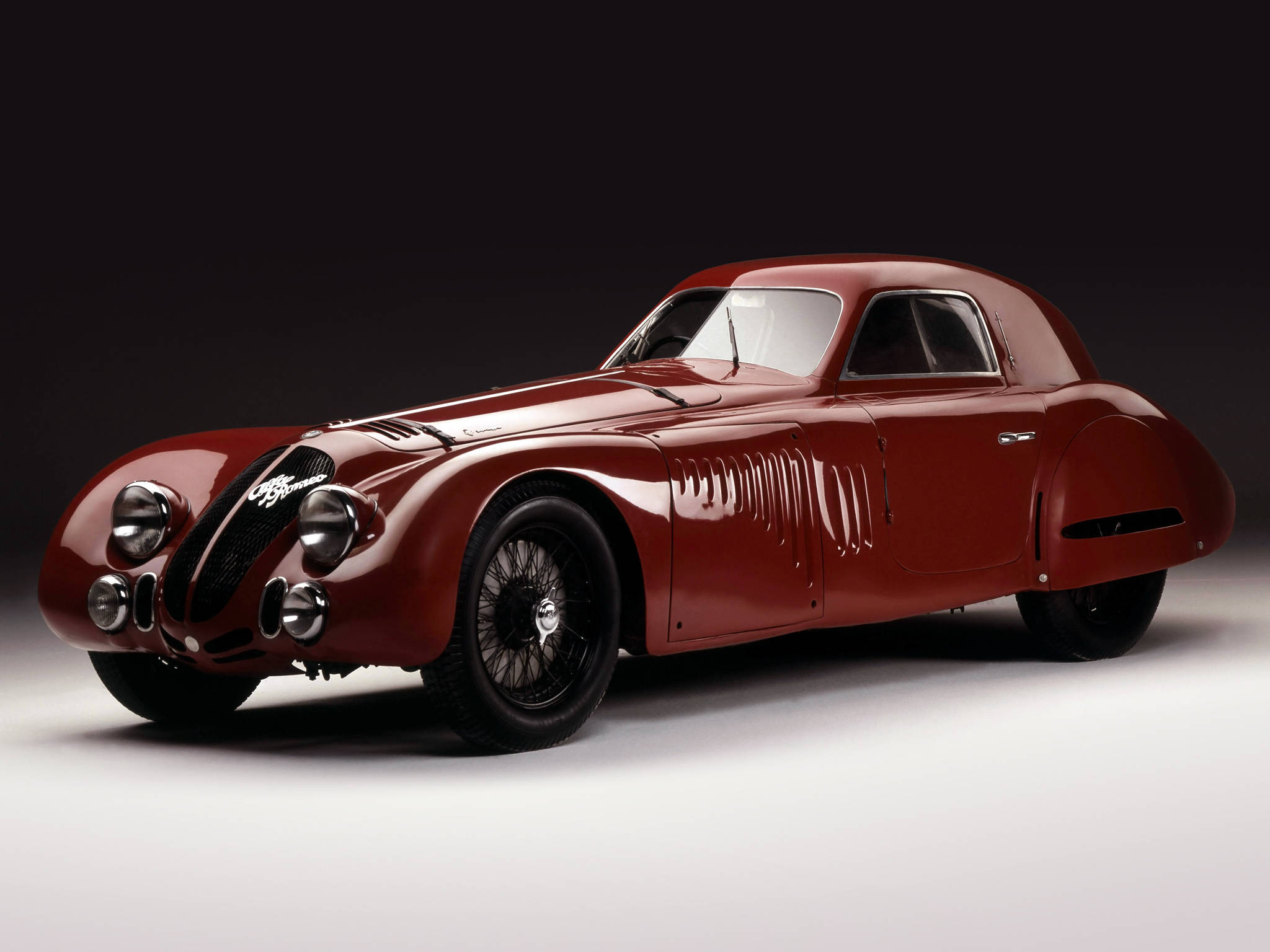 alfa romeo iPhone 桌布 壁紙 — 一輛光澤深紅色的復古愛快羅密歐賽車，帶有鍍鉻裝飾和鋼絲輪，置於深色漸變背景前。