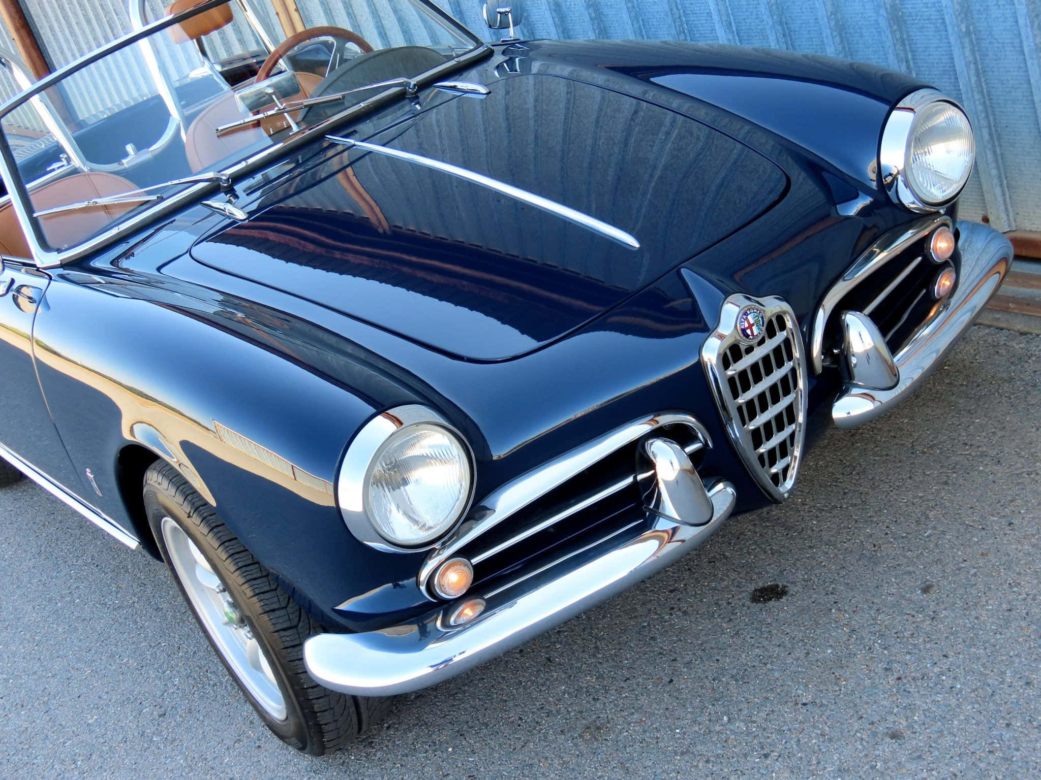 Alfa Romeo Spider 桌布 壁紙 — 一輛光澤深藍色經典愛快羅密歐Spider敞篷車在明亮日光下閃耀，帶有鍍鉻飾邊和可見的米色內飾。