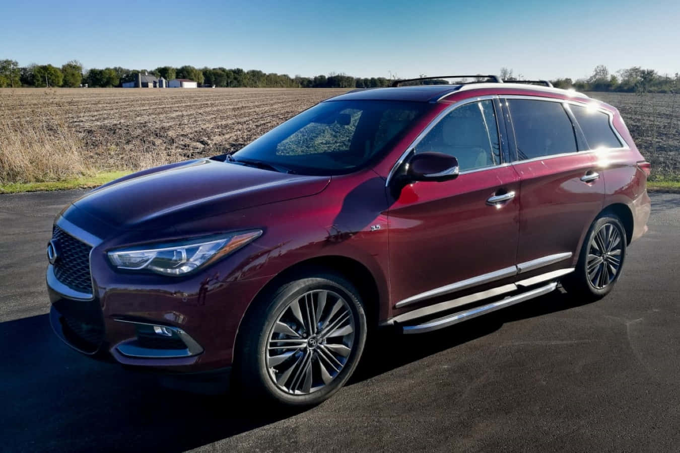 Infiniti Qx60 桌布 壁紙 — 一輛光澤的栗色Infiniti QX60 SUV停在瀝青路上，背景是收割後的田野和樹木，天空清澈湛藍。