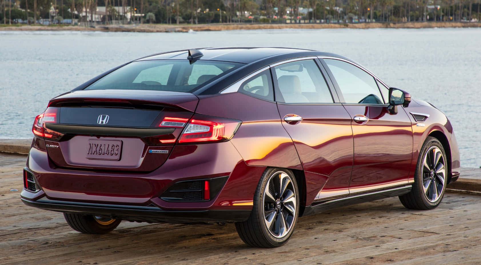 Honda Clarity 桌布 壁紙 — 一輛光澤的栗色本田Clarity插電式混合動力轎車停在木製碼頭上，旁邊是金色時刻的平靜水面。