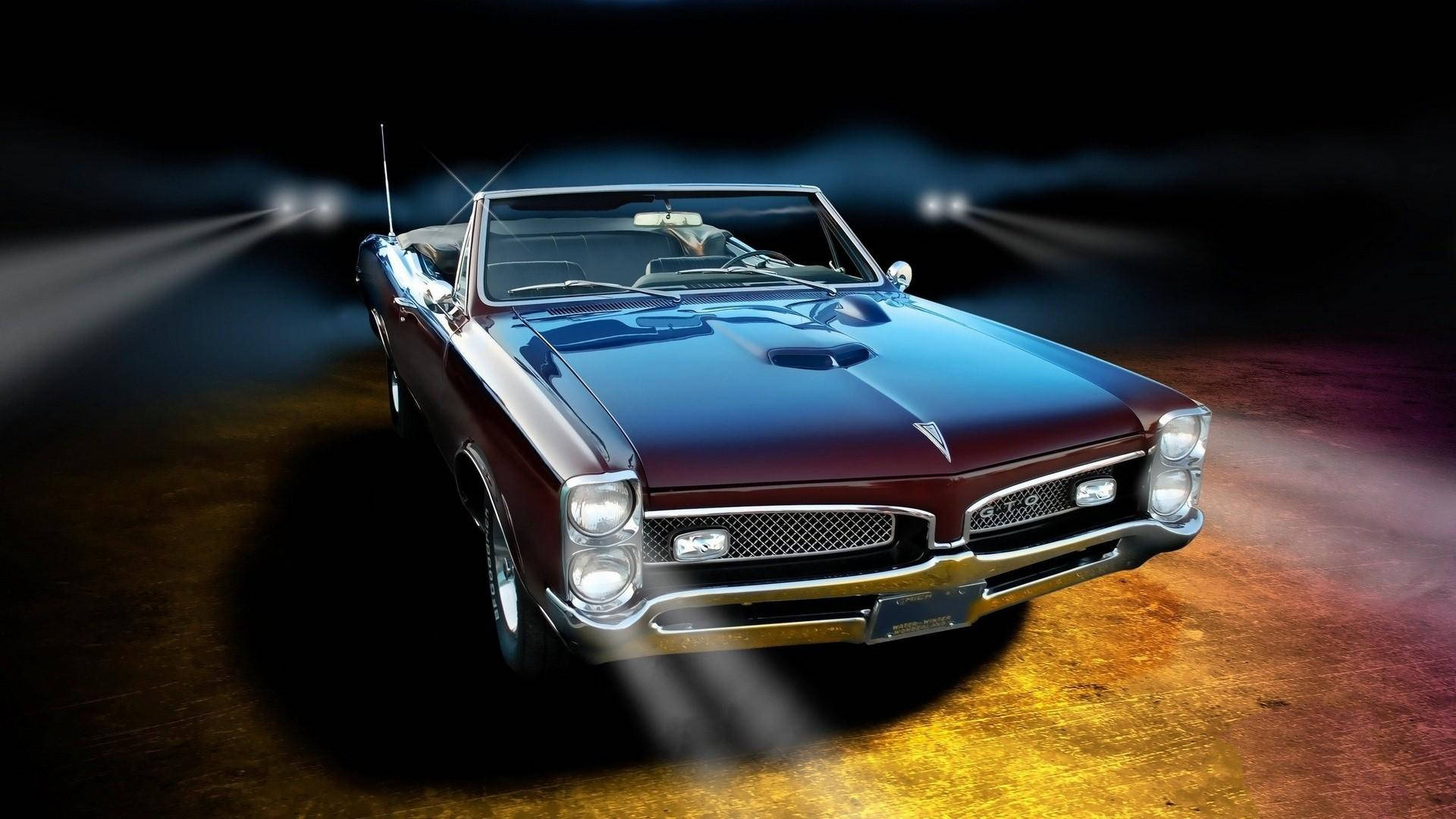 Pontiac 桌布 壁紙 — 一輛光澤的栗色經典敞篷肌肉車在黑暗的舞台上被聚光燈戲劇性地照亮，並帶有色彩繽紛的地板反射。